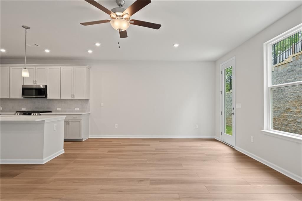 Modern open-concept kitchen with white cabinets, island, hardwood floors, ceiling fan, and backyard view in Davidson Homes The Marion B, Kennesaw, GA