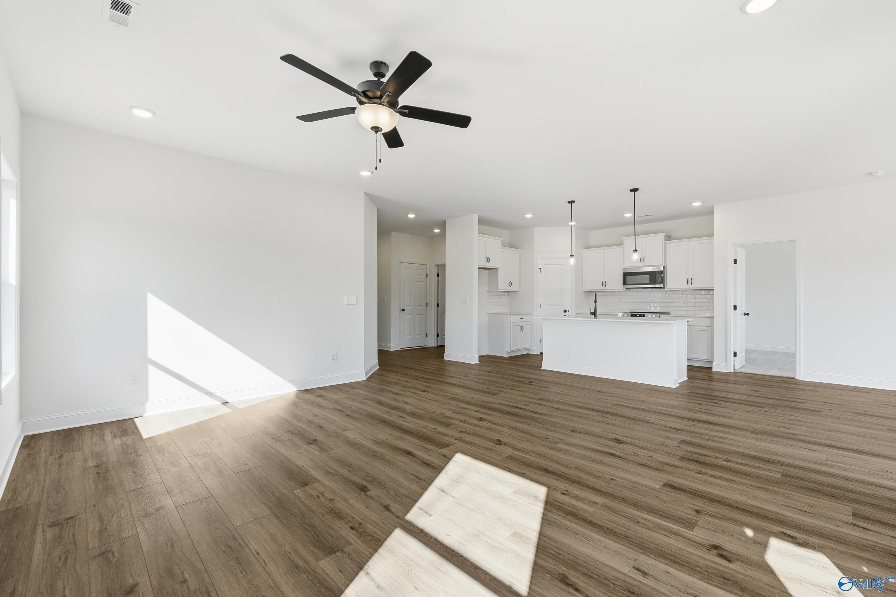 Open-concept living kitchen with white cabinets, island, ceiling fan, and hardwood floors in Davidson Homes The Franklin C, New Market, AL