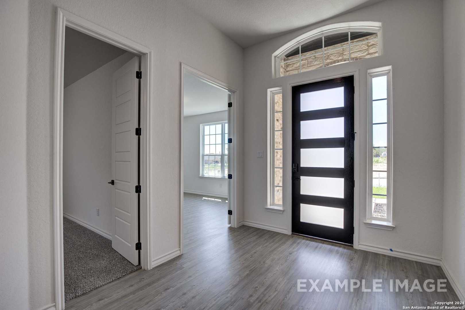Grand entry foyer with black frosted glass door, arched window, and open hallways in The Garner C, Castroville, Texas