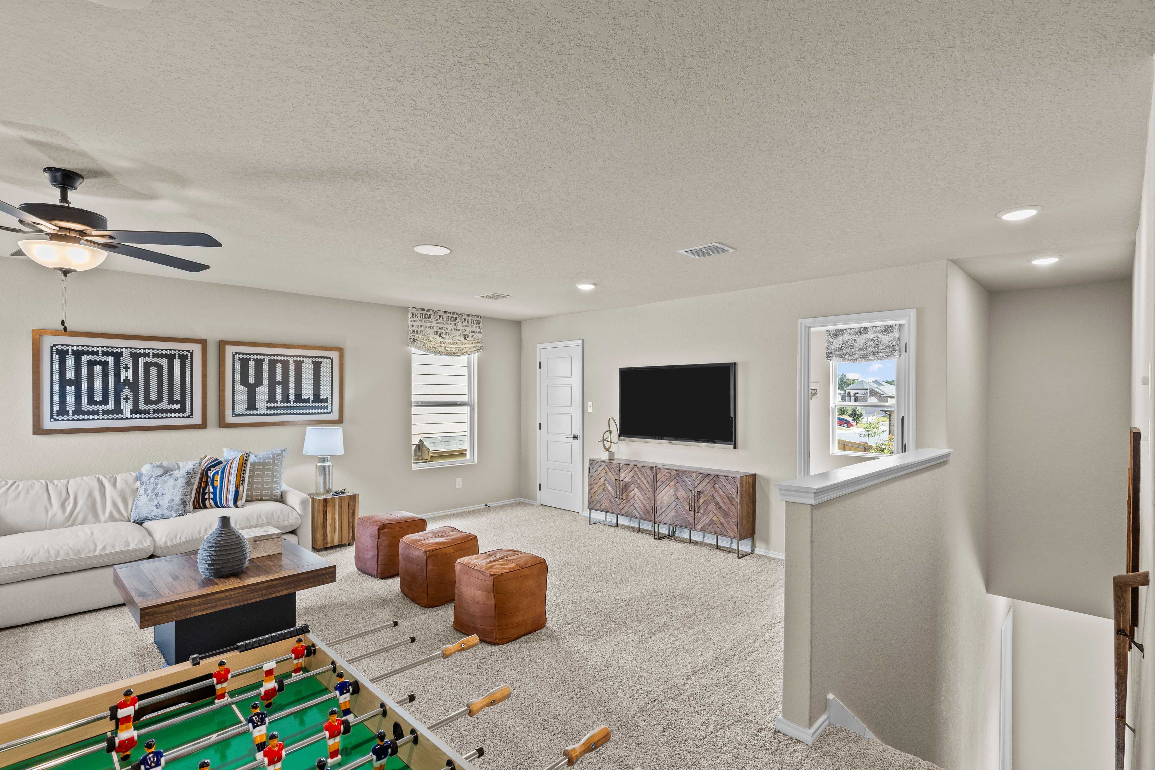 Spacious game room at Bricewood in San Antonio TX with foosball table, beige sofa, TV console and ceiling fan