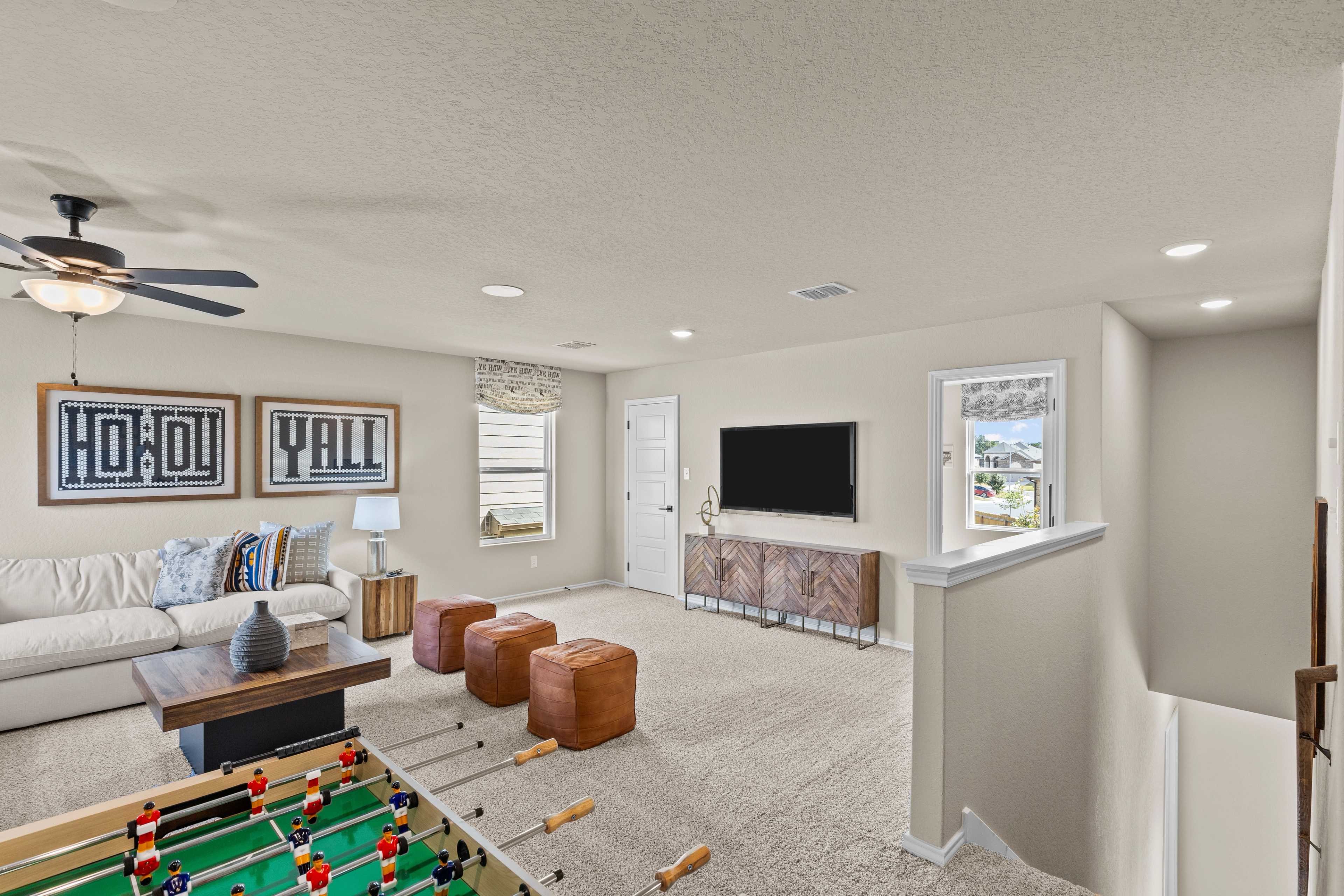 Spacious game room at Bricewood in San Antonio TX with foosball table, beige sofa, TV console and ceiling fan