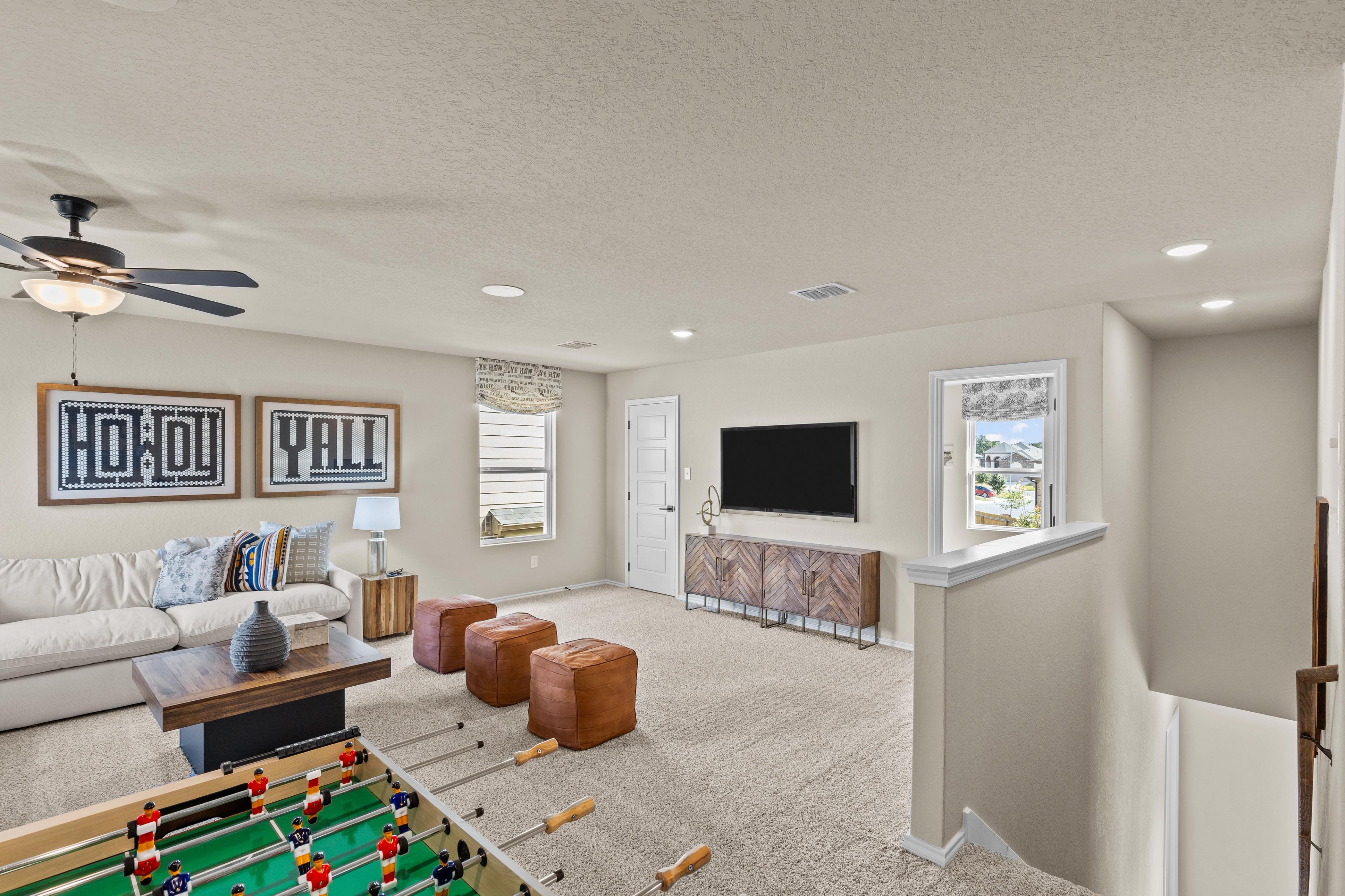 Spacious game room at Bricewood in San Antonio TX with foosball table, beige sofa, TV console and ceiling fan