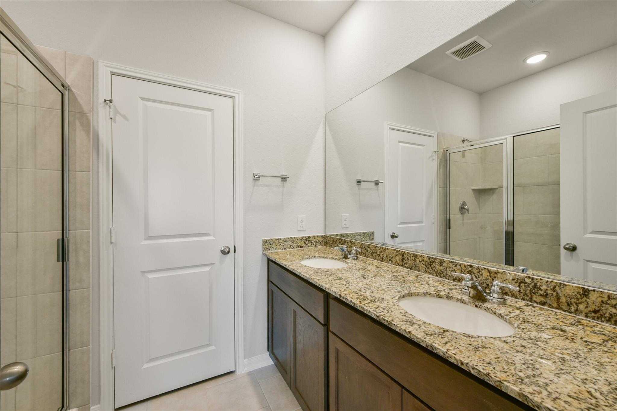 Elegant master bathroom with double granite vanity, large mirrors, and glass shower in Davidson Homes Sabine E, Dayton, Texas