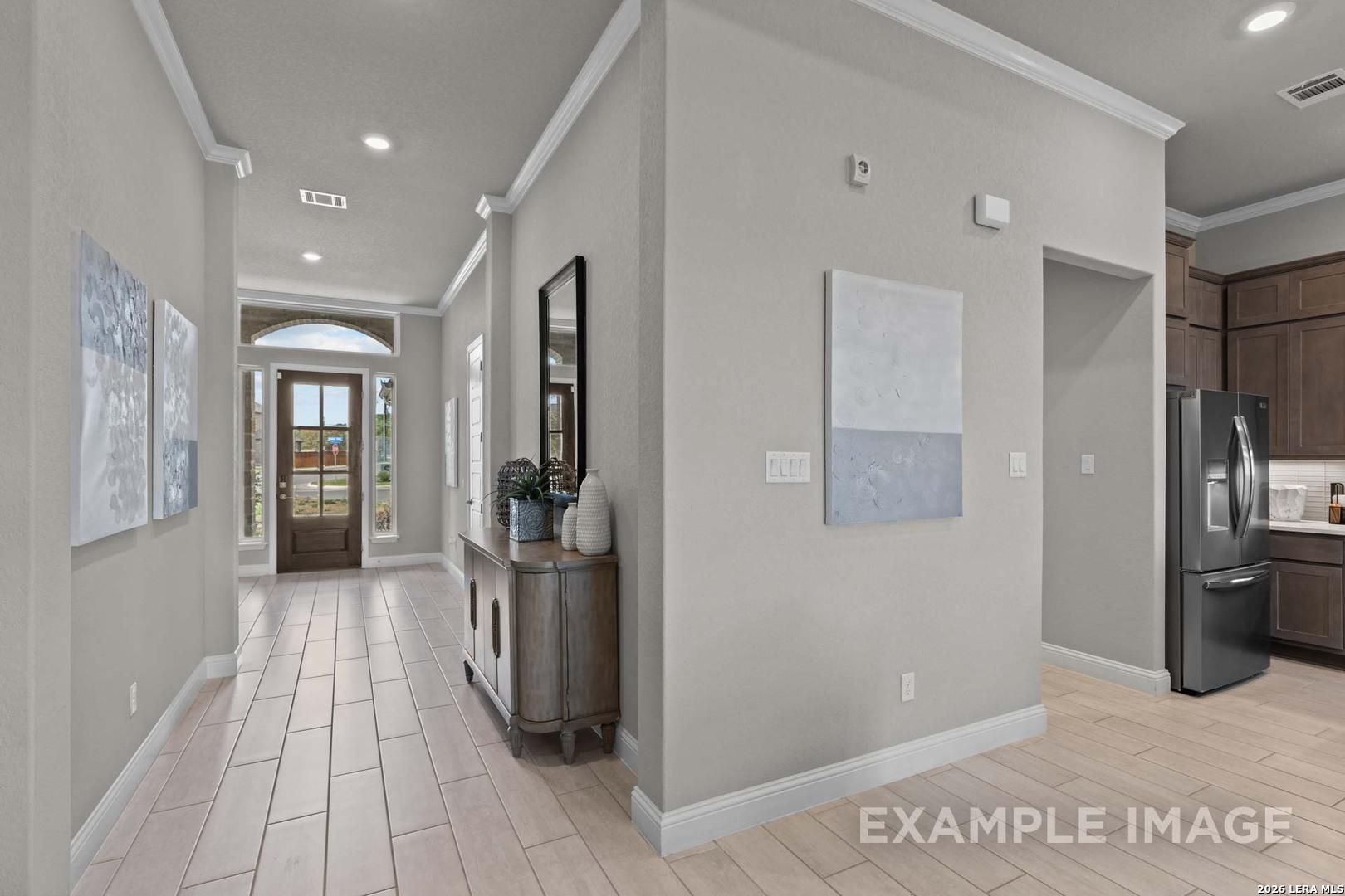 Bright entryway with wood-look tile flooring leading to kitchen in The Garner C floor plan at The Reserve at Potranco Oaks.
