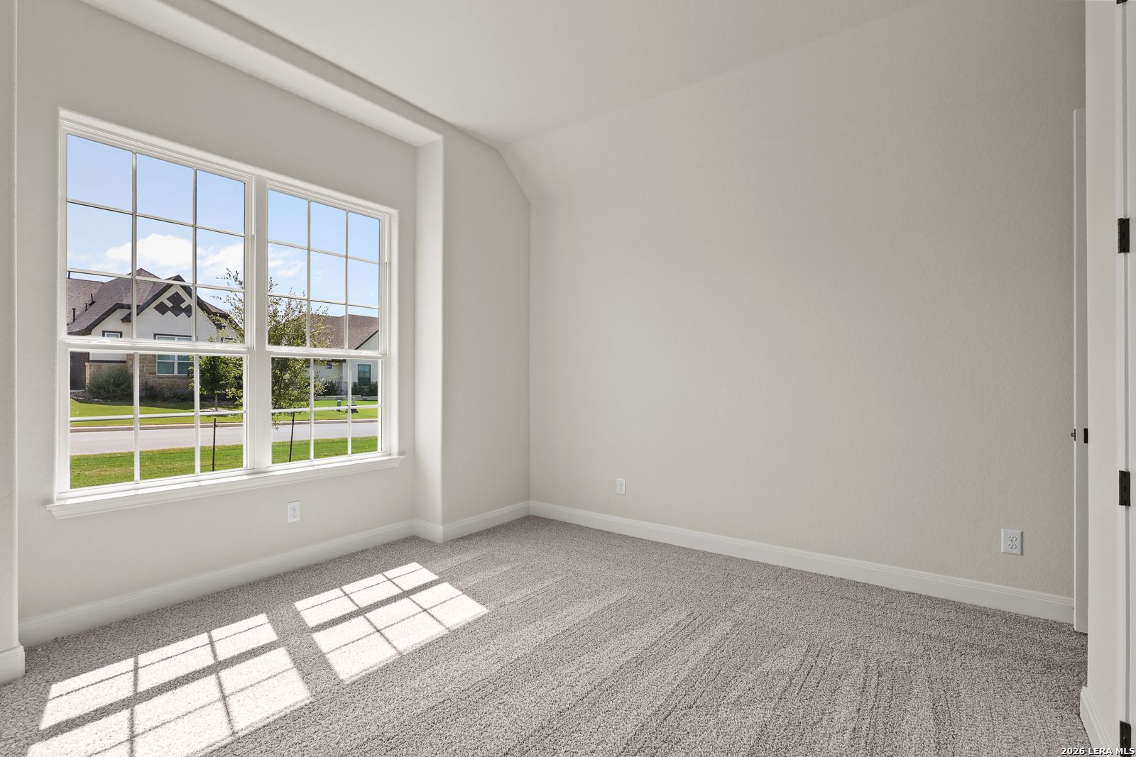 Bright, carpeted bedroom with large window in The Summerlin B floor plan at Potranco Oaks, Castroville, Texas.