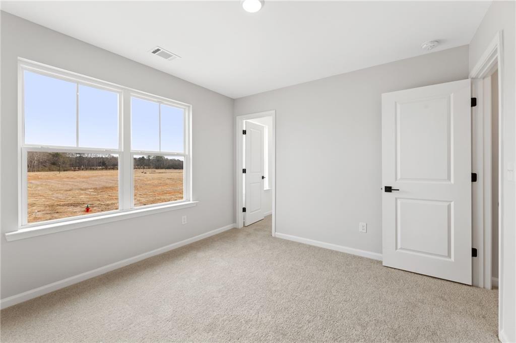 Bright bedroom with large windows overlooking rural fields, gray walls, and carpeted floor in Davidson Homes The Rabun C, Winder, Georgia