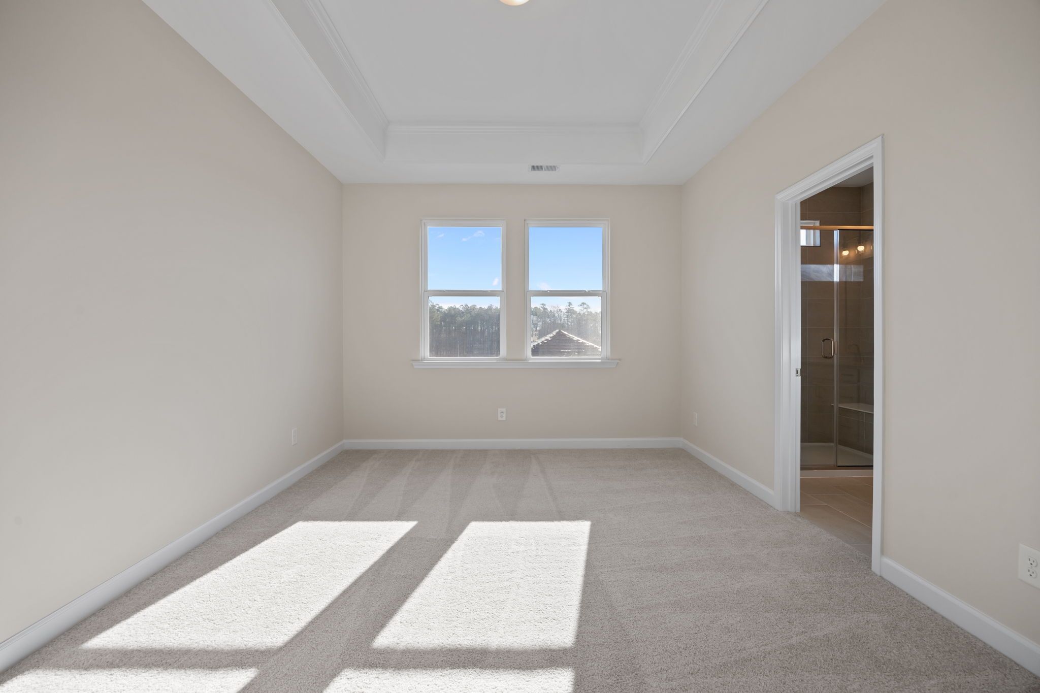 Spacious bedroom with tray ceiling and en-suite bathroom at Forestville Yard in Knightdale, NC by Davidson Homes.