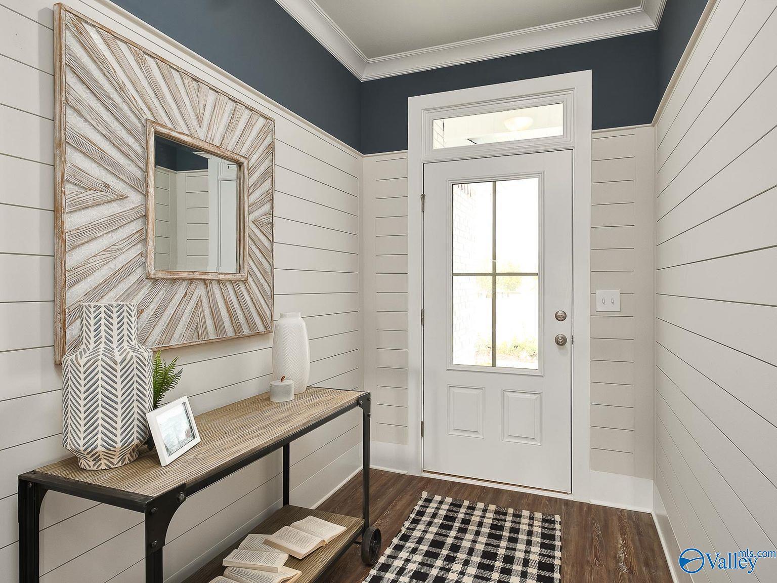 Bright entryway featuring shiplap walls, large framed mirror, metal console table, and glass exterior door in The Everett 4-bedroom home, Toney, Alabama