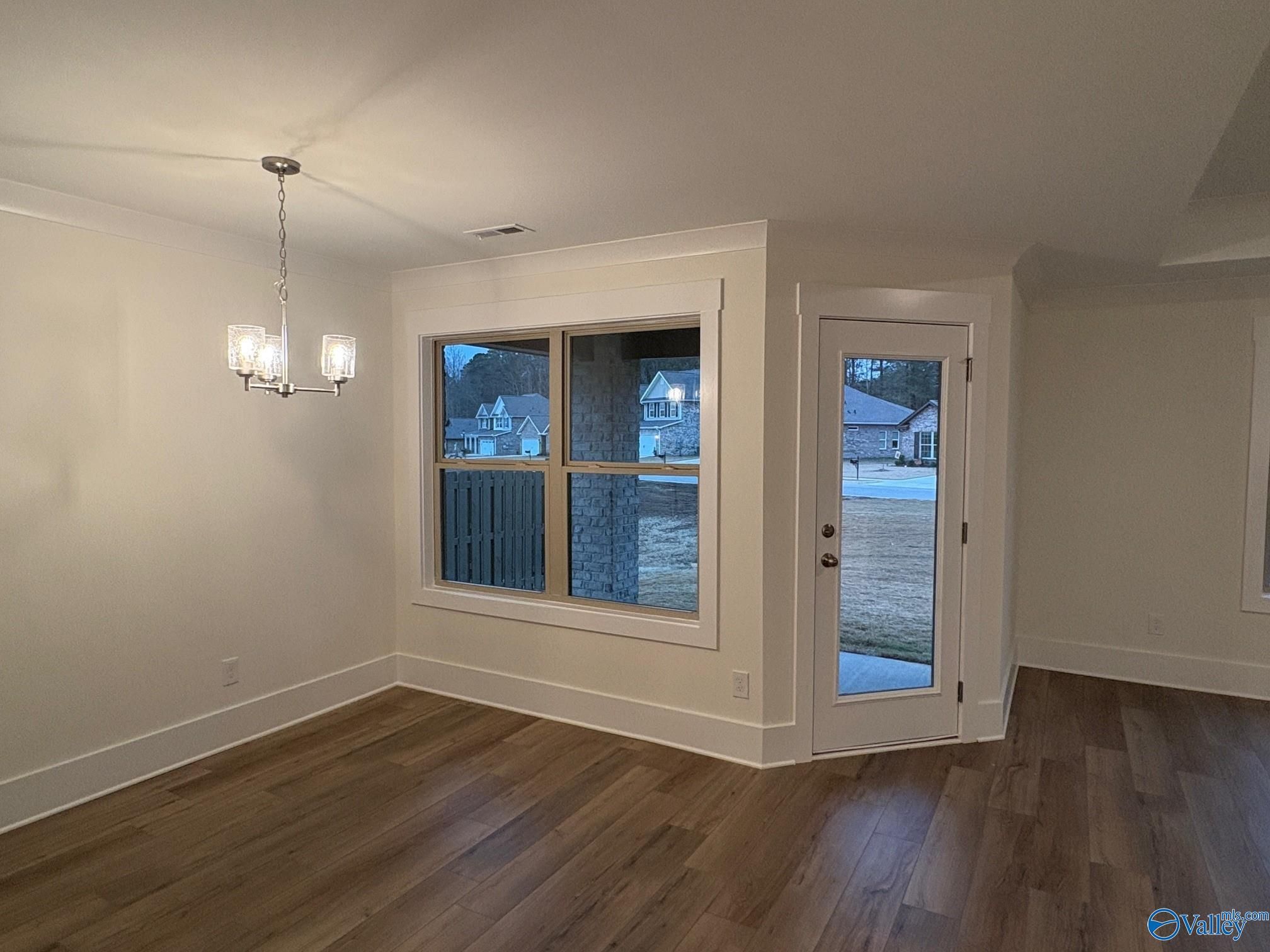 Bright living room with hardwood floors, modern chandelier, large triple window, and glass door to snowy backyard in The Daphne C home, Arab, Alabama