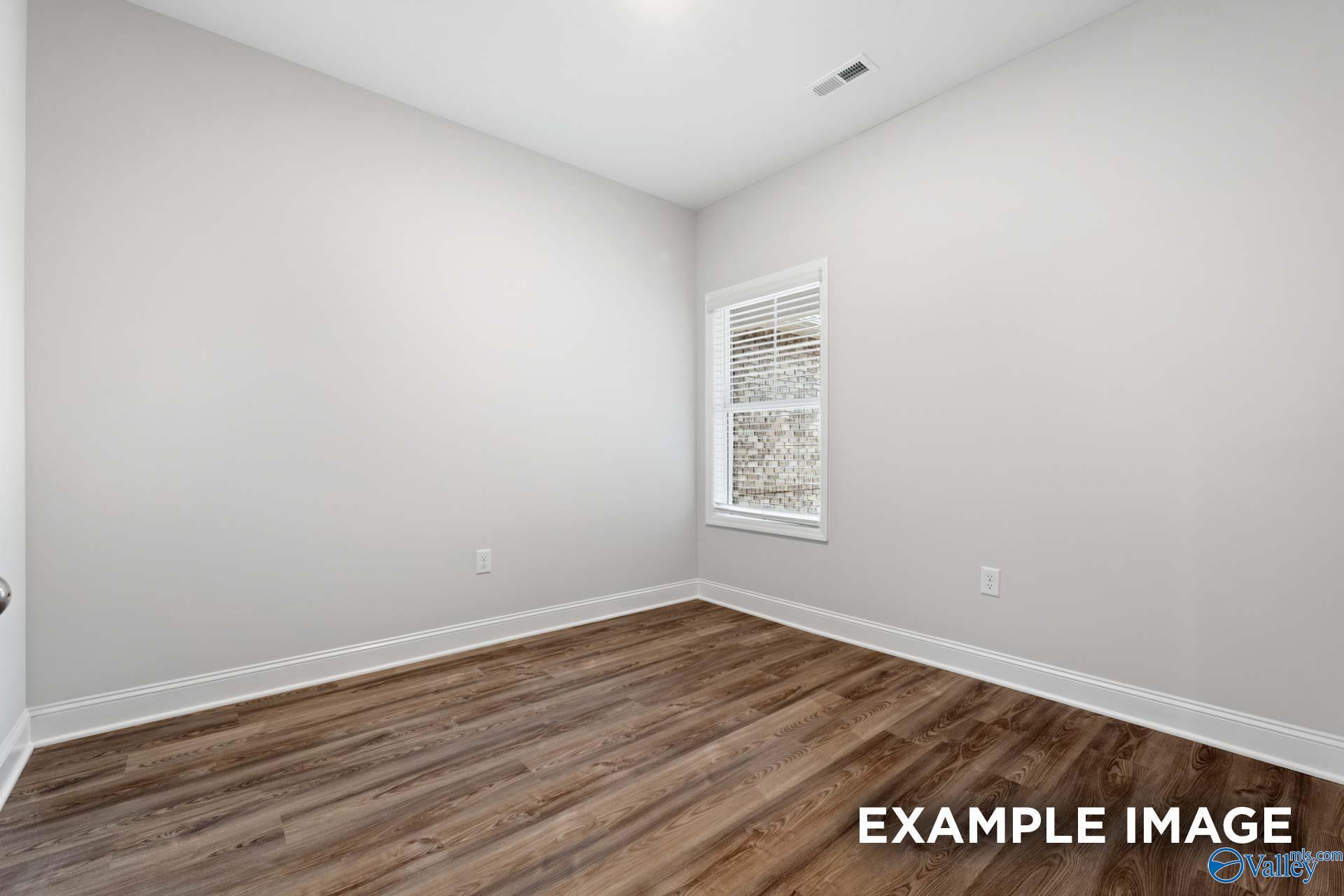 Bright secondary bedroom featuring light gray walls, hardwood floors, and window with blinds in Davidson Homes The Cumberland, Decatur, Alabama