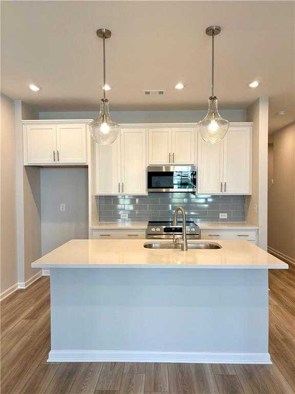 Modern white kitchen with quartz island, stainless appliances, subway tile backsplash, and pendant lights in Davidson Homes The Monroe A, Emerson, GA