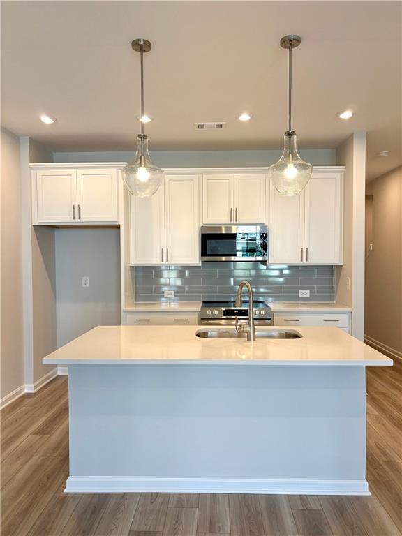 Modern white kitchen with quartz island, stainless appliances, subway tile backsplash, and pendant lights in Davidson Homes The Monroe A, Emerson, GA