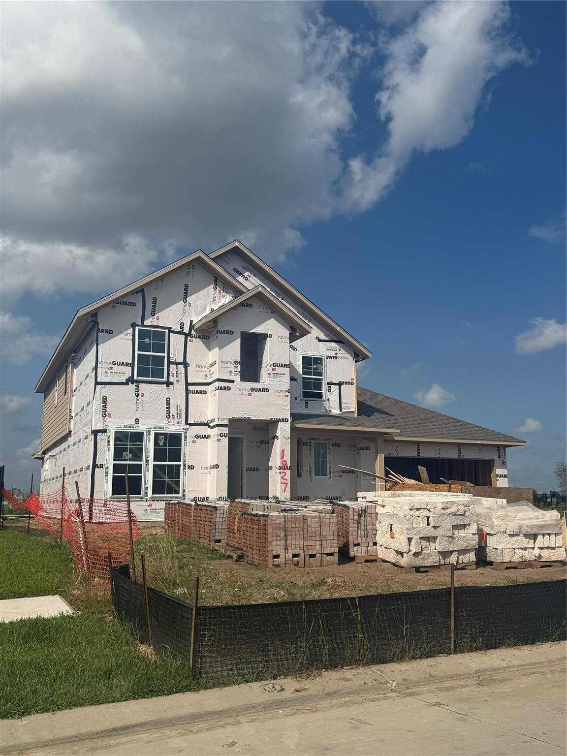 Partially constructed 4-bedroom Philip C home by Davidson Homes in Sierra Vista, Rosharon, Texas, with house wrap, windows, and stacked brick pallets
