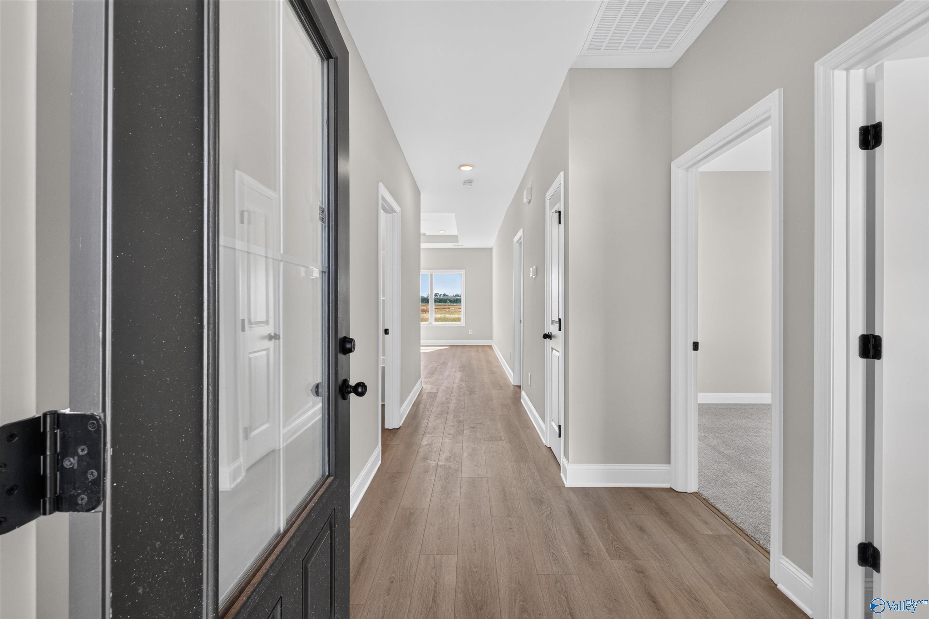 Foyer with black glass-panel front door, hardwood floors, and neutral hallway leading to bedrooms in Davidson Homes' The Butler plan