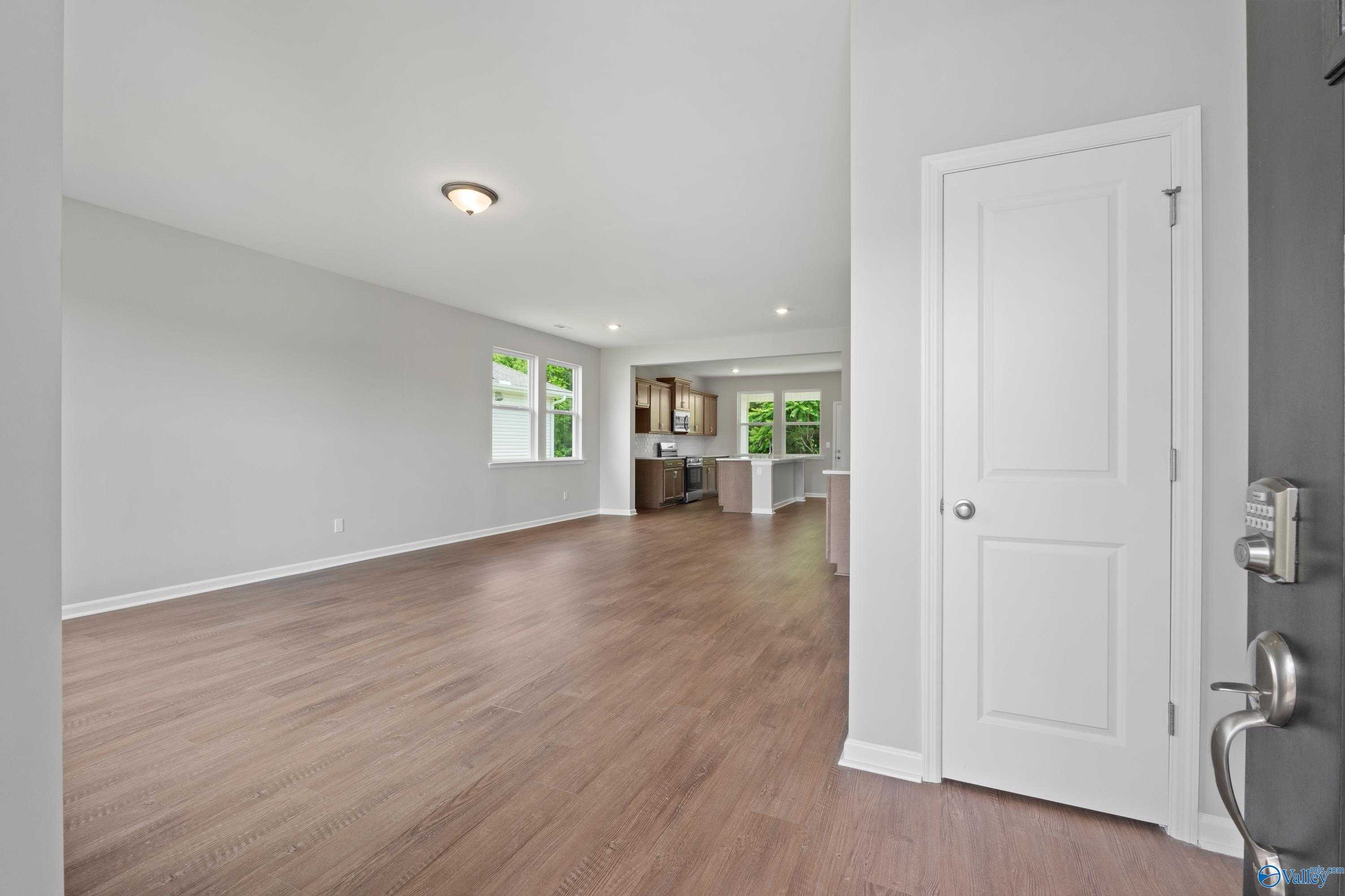 Open-concept living space with hardwood floors, white cabinetry kitchen, and natural light in The Stella 3-bedroom home, Hazel Green, Alabama
