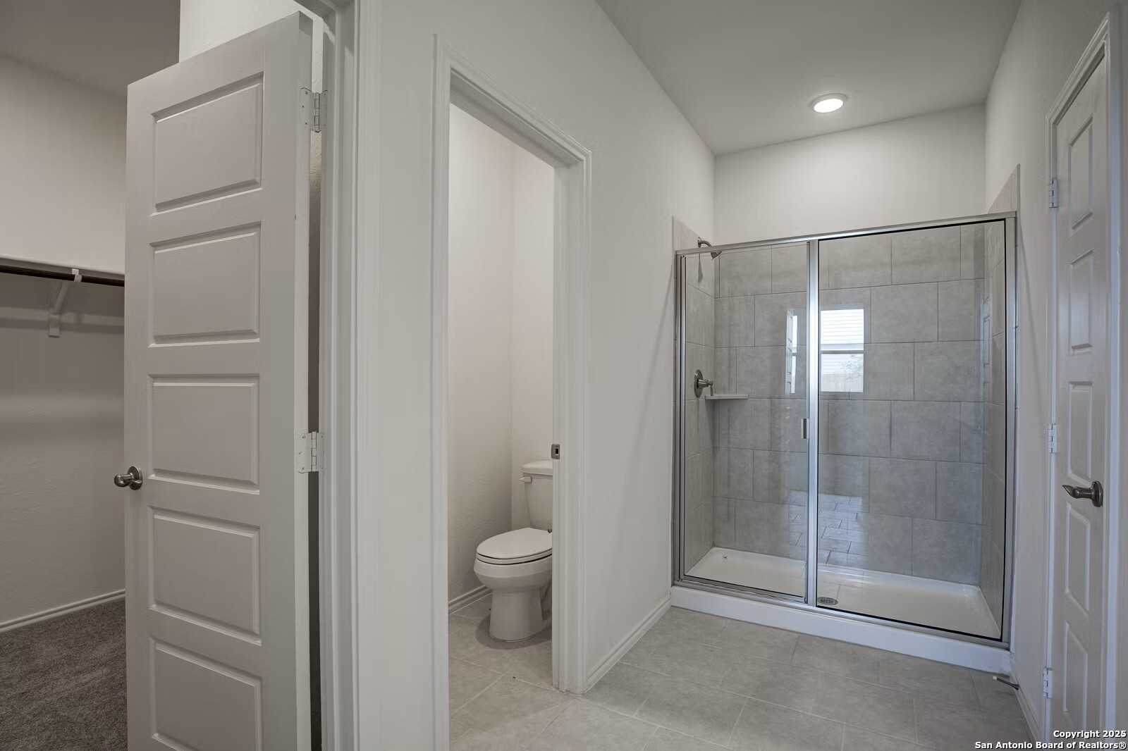 Modern master bathroom featuring frameless glass walk-in shower, white toilet, and built-in closets in Davidson Homes Douglas B, Seguin, Texas