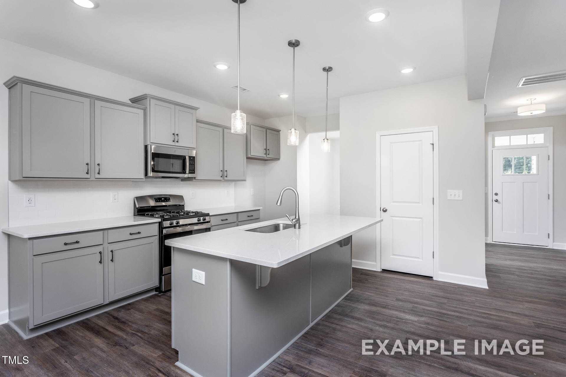 Modern gray kitchen with large island, stainless appliances, pendant lights in The Willow B floor plan, Lillington, NC