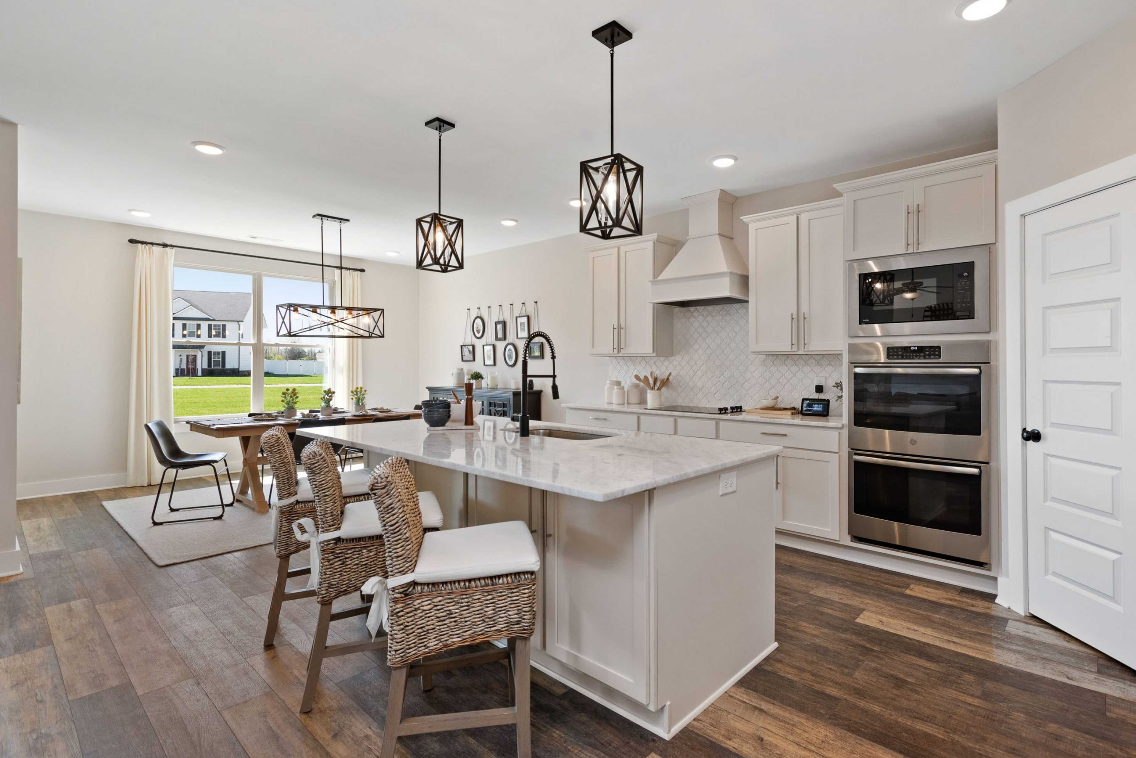 Spacious open-concept kitchen at Rivers Edge in Murfreesboro TN with white cabinets, quartz island, stainless appliances, and hardwood floors