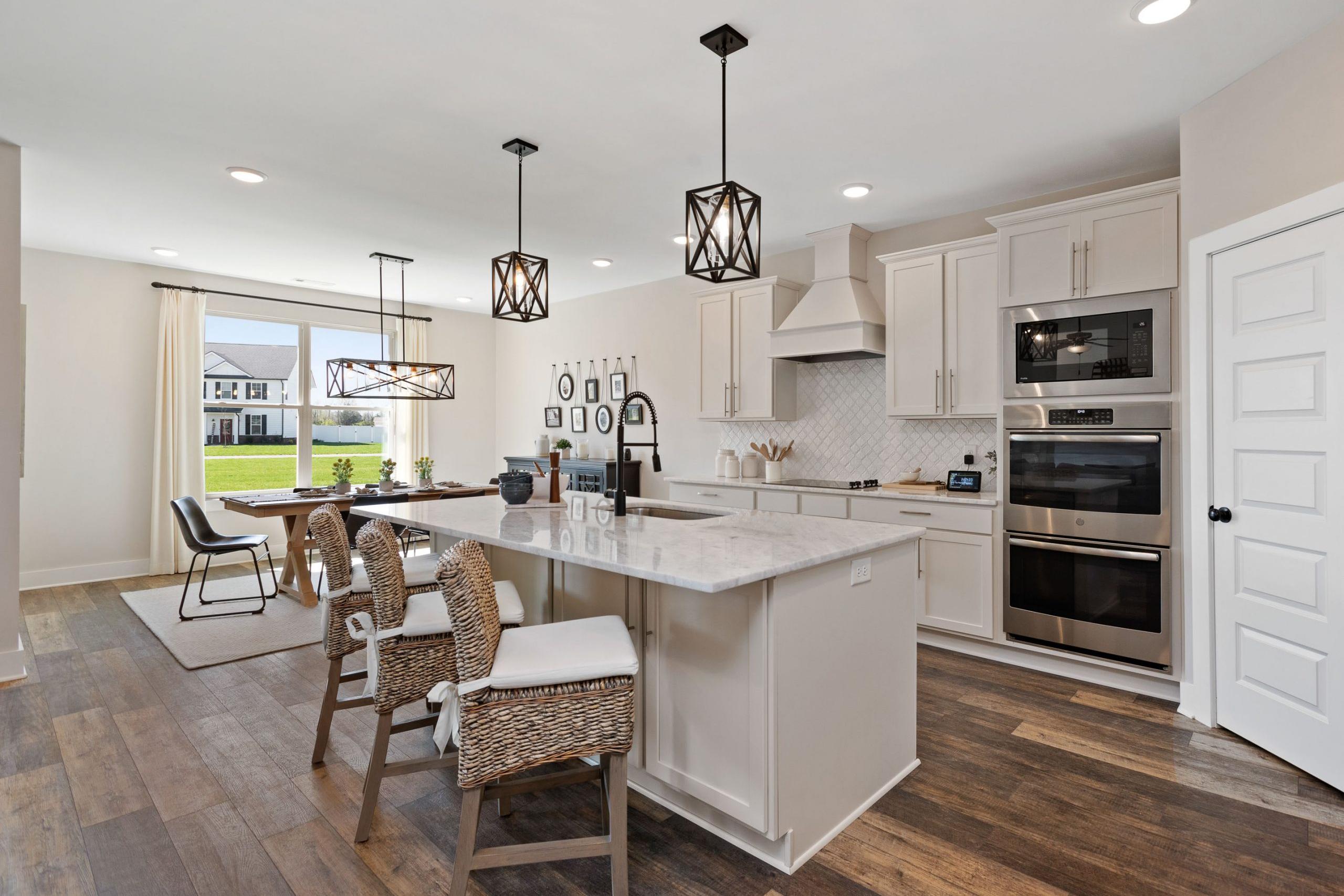 Spacious open-concept kitchen at Rivers Edge in Murfreesboro TN with white cabinets, quartz island, stainless appliances, and hardwood floors