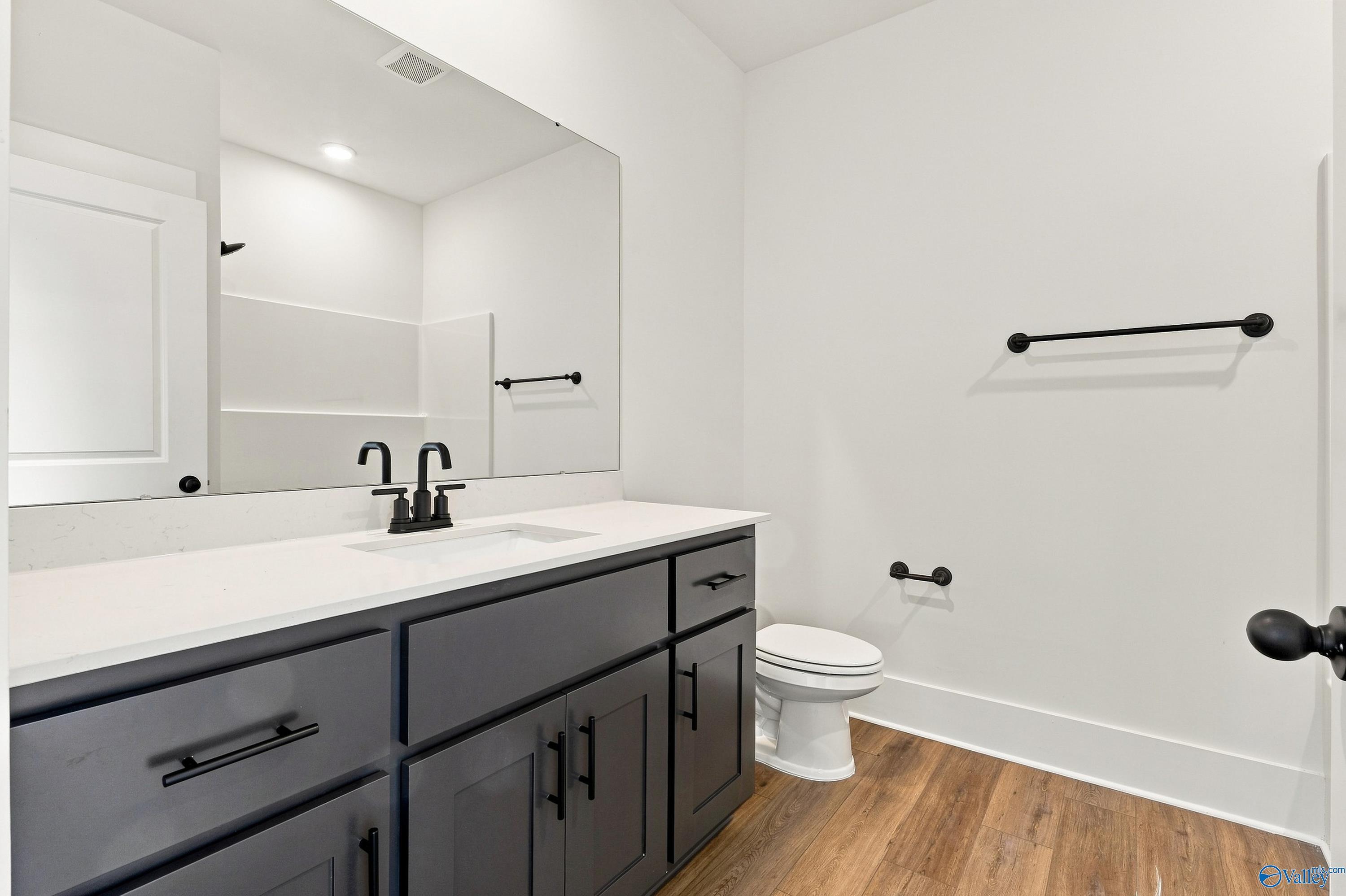 Modern bathroom with dark gray vanity, white quartz countertop, black fixtures, and hardwood floors in The Valencia, Huntsville