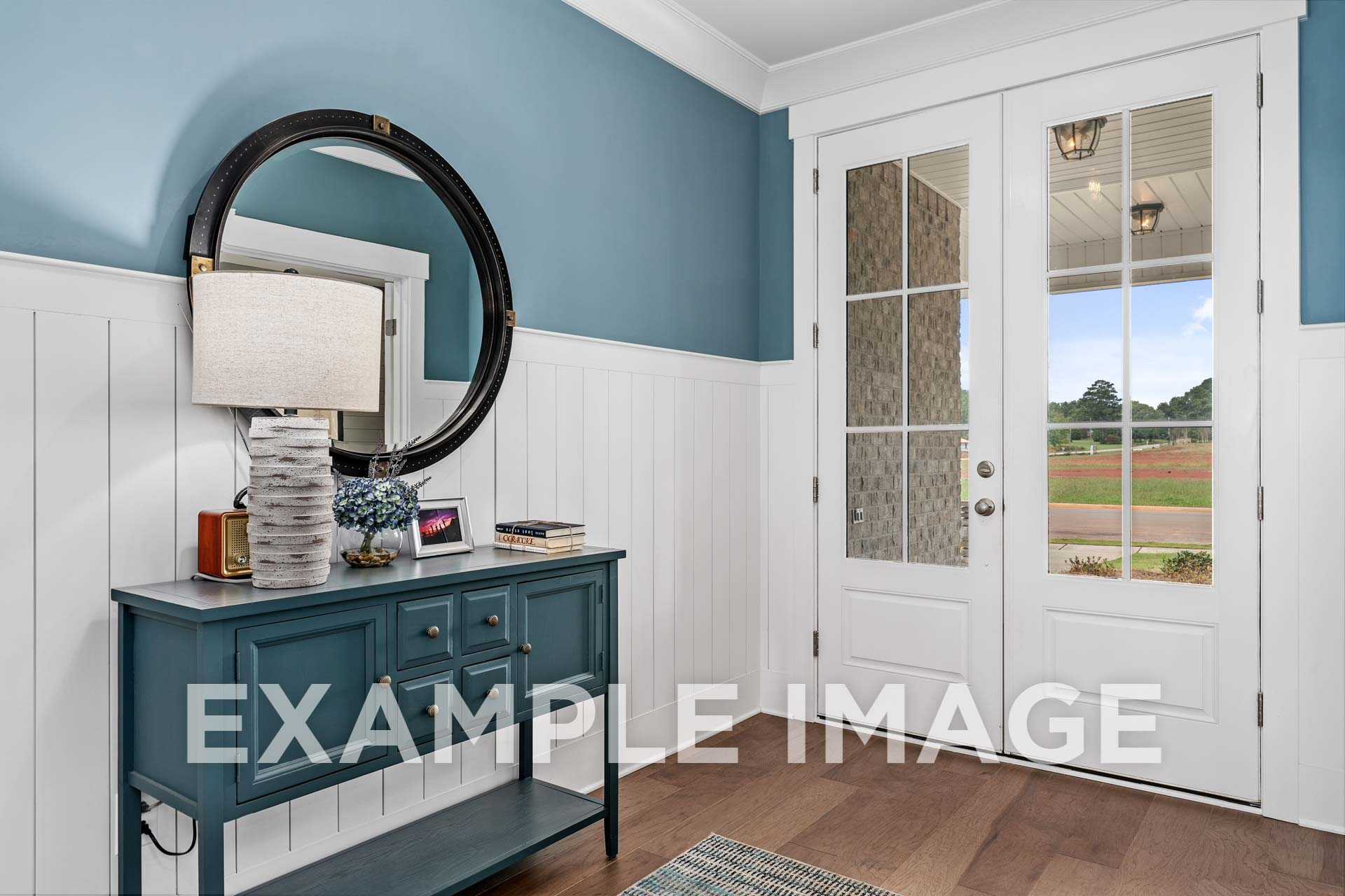 Elegant entryway in The Harrison D home design featuring teal walls, round mirror, console table with decor, and French doors to scenic view