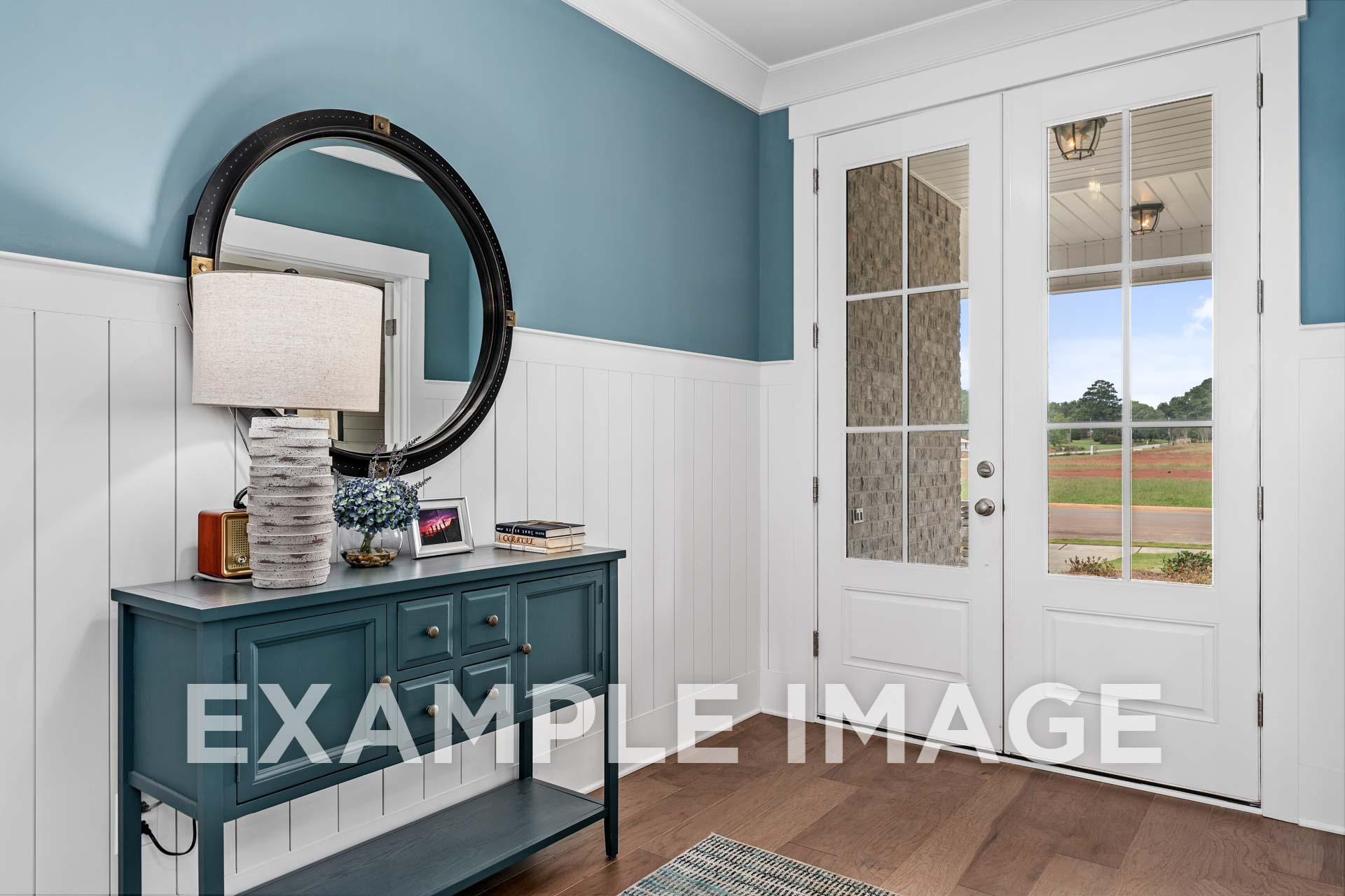 Elegant entryway in The Harrison home by Davidson Homes: teal walls, wainscoting, console table with round mirror, lamp and decor, double glass doors to scenic fields view