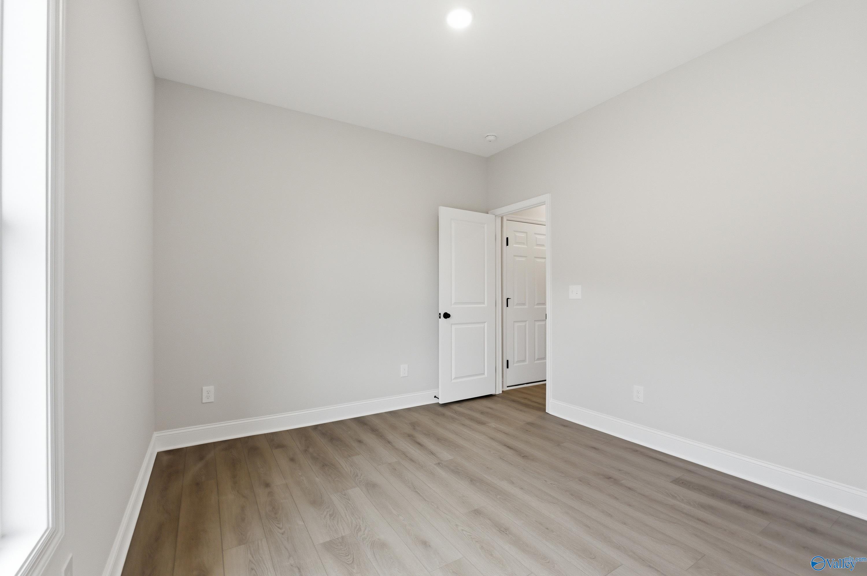 Spacious empty bedroom with light gray walls, white doors, and hardwood floors in Davidson Homes The Daphne C, Huntsville, Alabama
