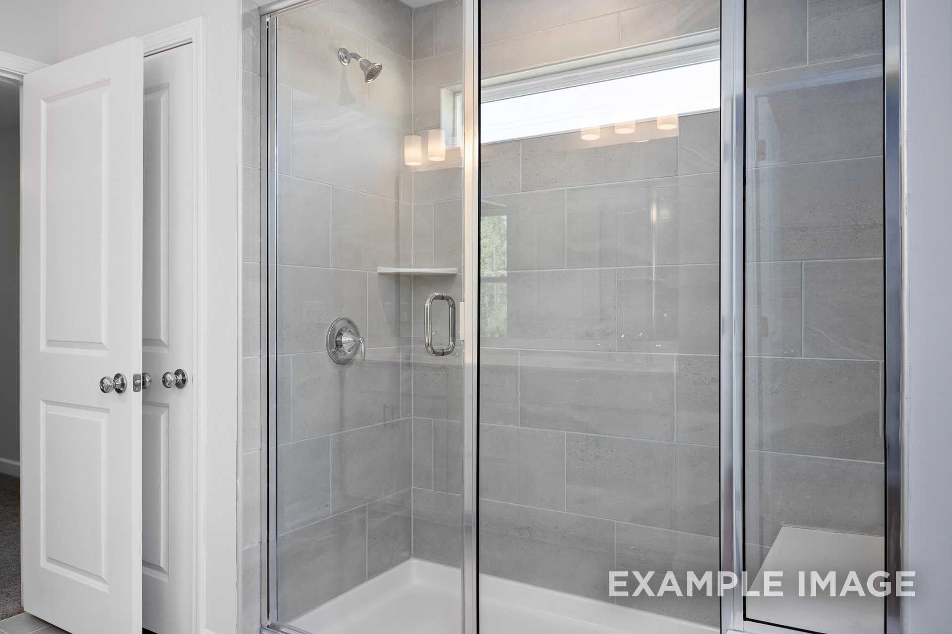 Spacious frameless glass shower in The Gavin C master bath with gray subway tile walls and built-in niche