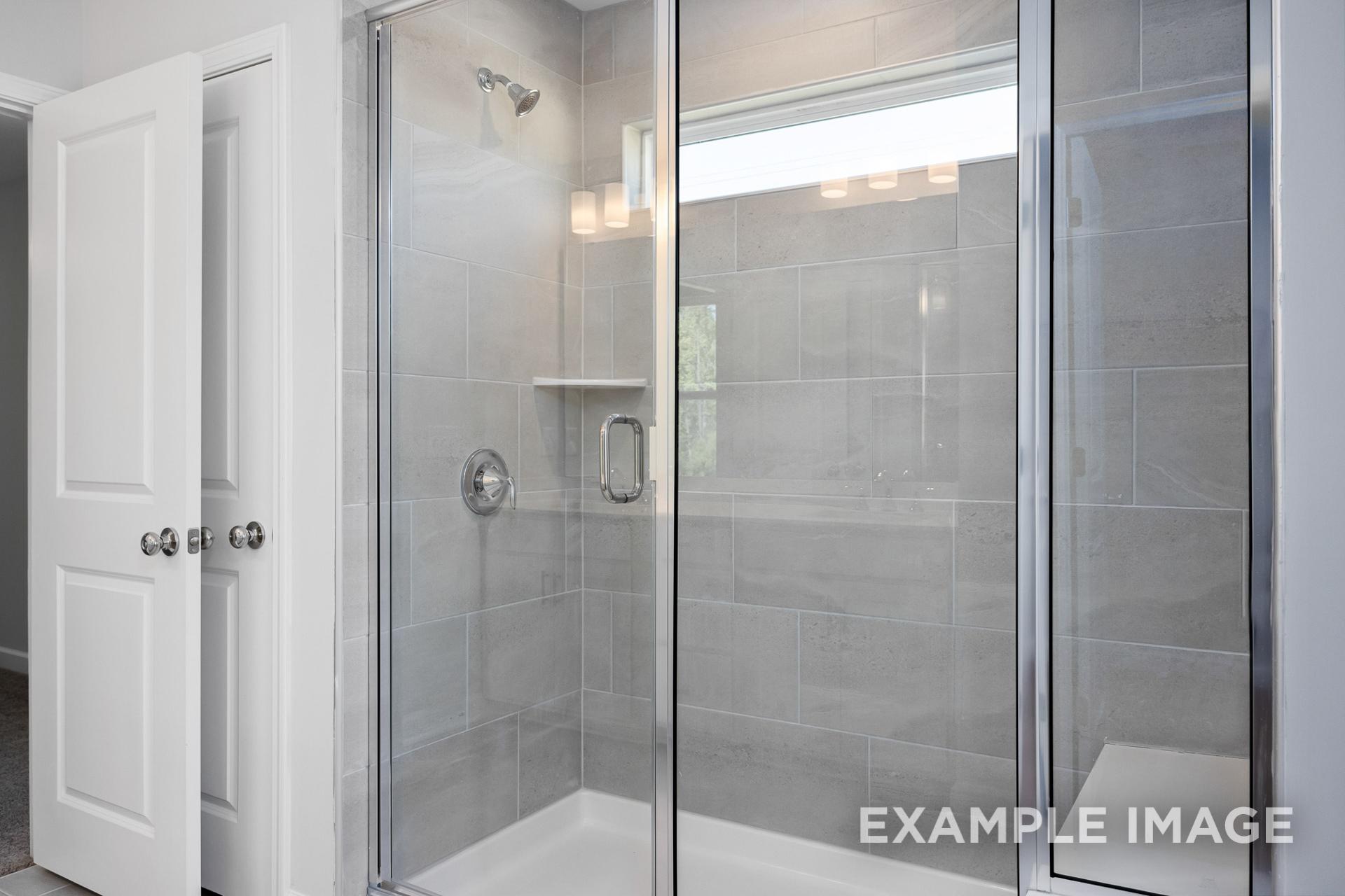 Modern walk-in shower in The Gavin B master bath with frameless glass doors, gray subway tiles, and niche shelf