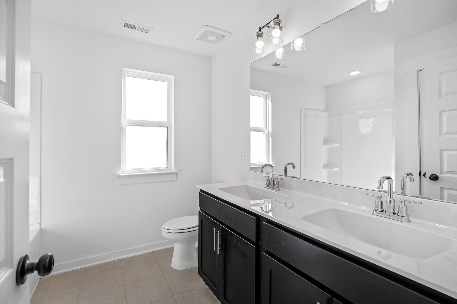 Modern double-sink vanity with black cabinets, white tiled tub, and large mirror in 5-bedroom Davidson Homes The Willow, Gallatin, Tennessee