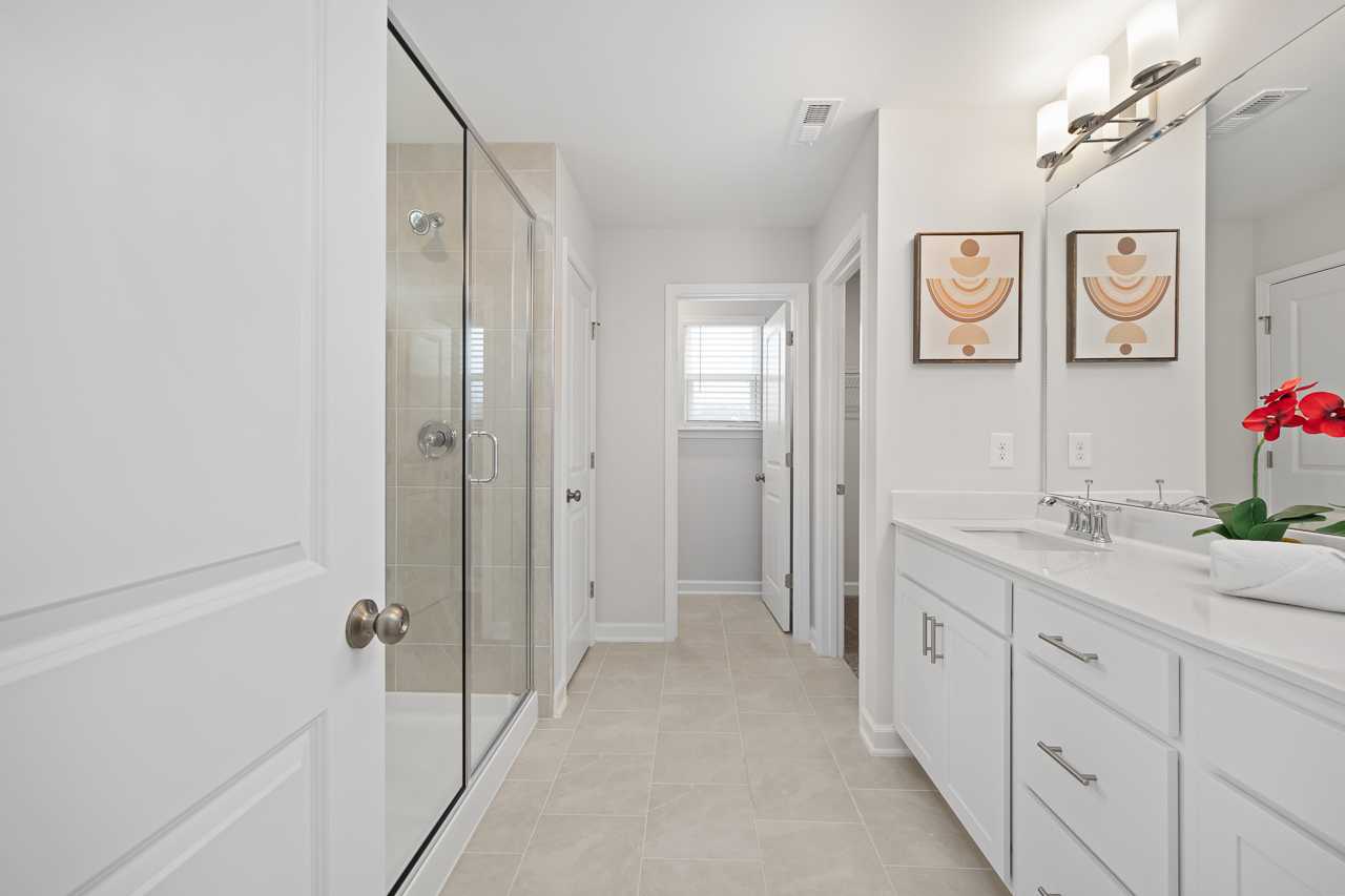 Spacious primary bathroom at Gregory Village in Lillington NC with frameless glass shower, white double vanity, and modern wall art