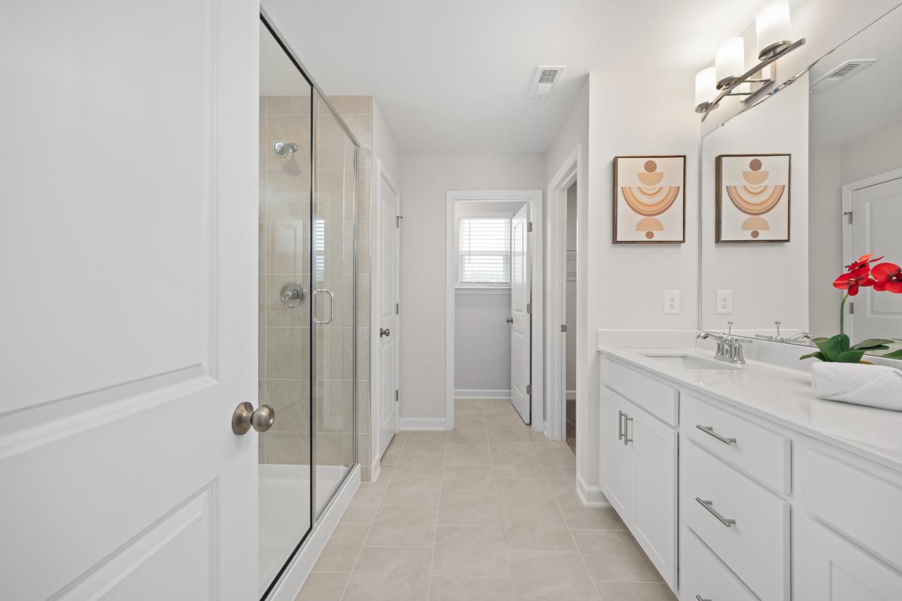 Spacious primary bathroom at Gregory Village in Lillington NC with frameless glass shower, white double vanity, and modern wall art