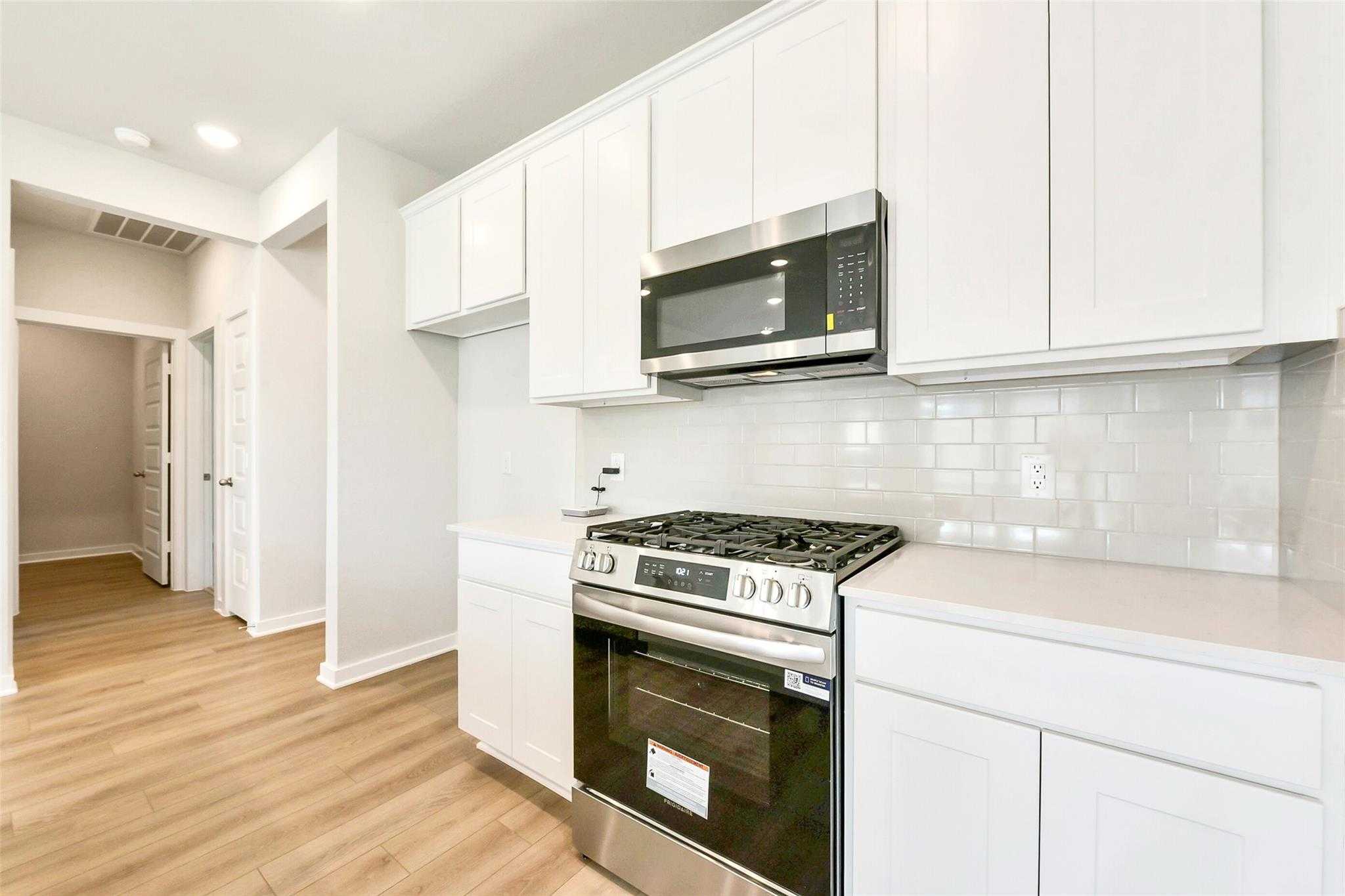 Modern white kitchen with stainless steel gas range, oven, and subway tile backsplash in Davidson Homes The Comal G, Dayton, Texas