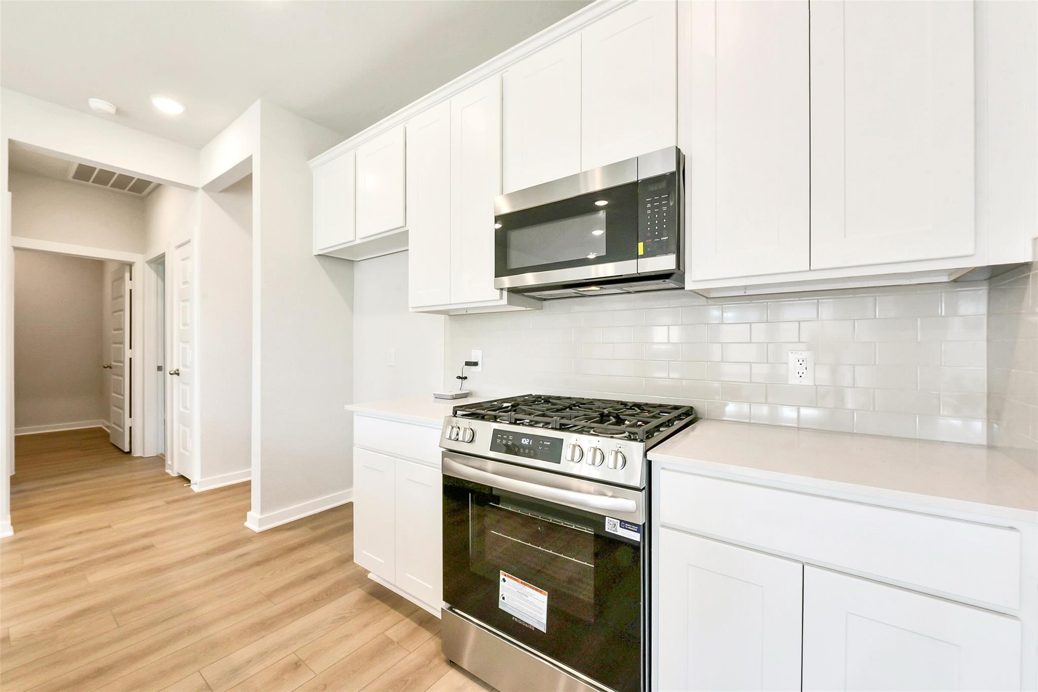 Modern white kitchen with stainless steel gas range, microwave, and subway tile backsplash in Davidson Homes The Comal G, Dayton, Texas