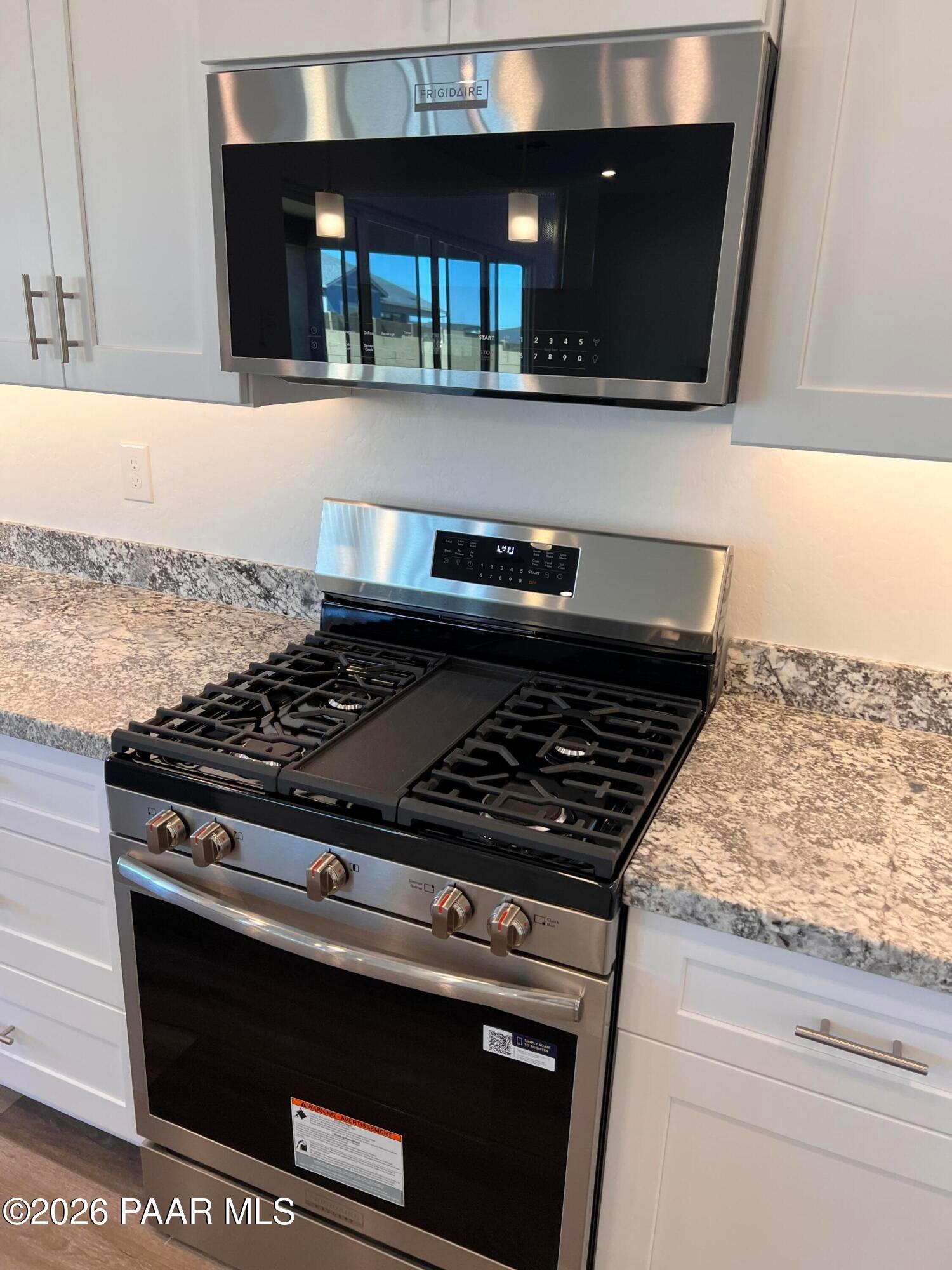 Modern kitchen featuring stainless steel gas range, microwave, and granite countertops in Davidson Homes The Sunrise II A, Prescott Arizona