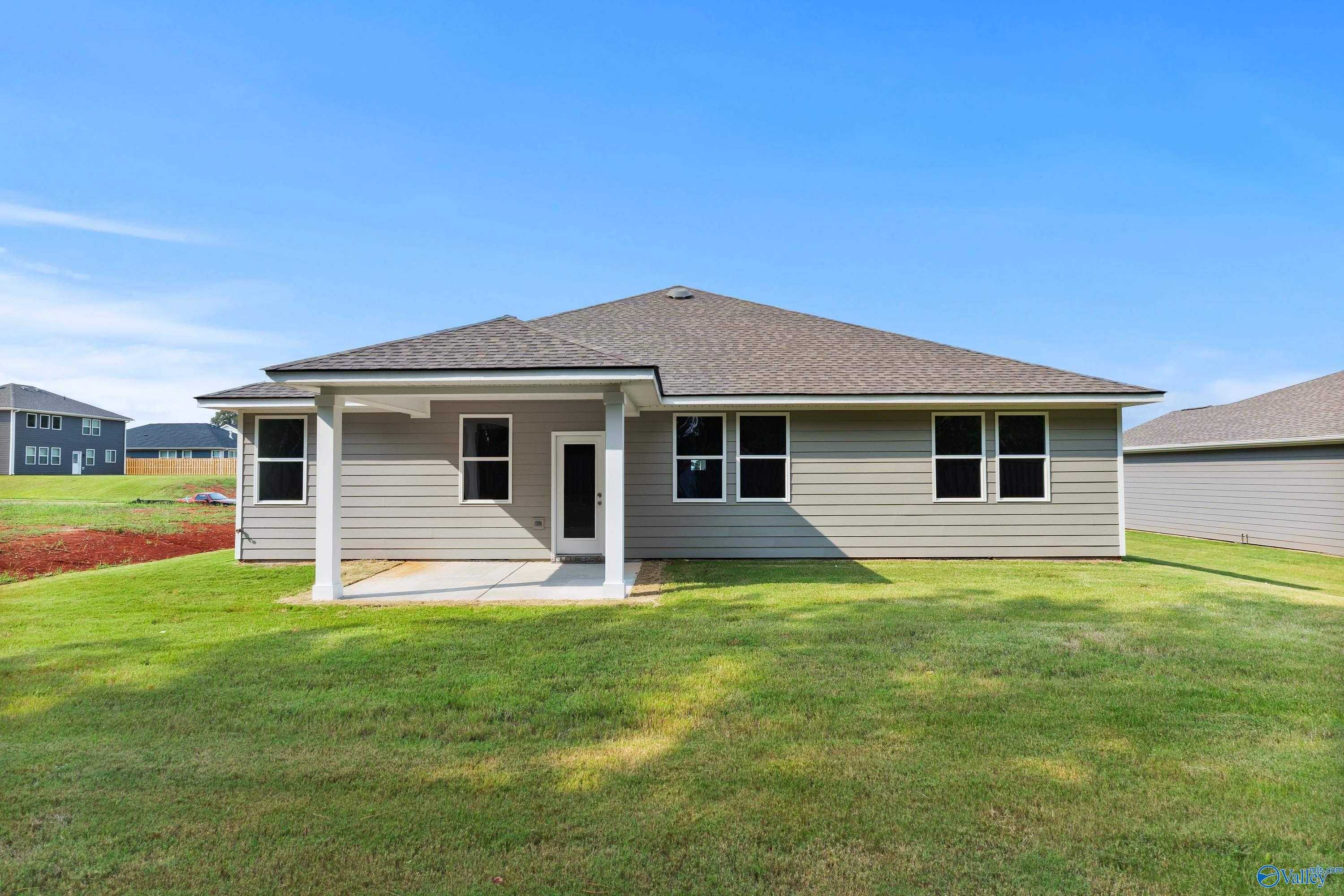 Rear view of single-story The Grace home with covered patio, columns, and lush green backyard in Evergreen Mill, Madison, Alabama