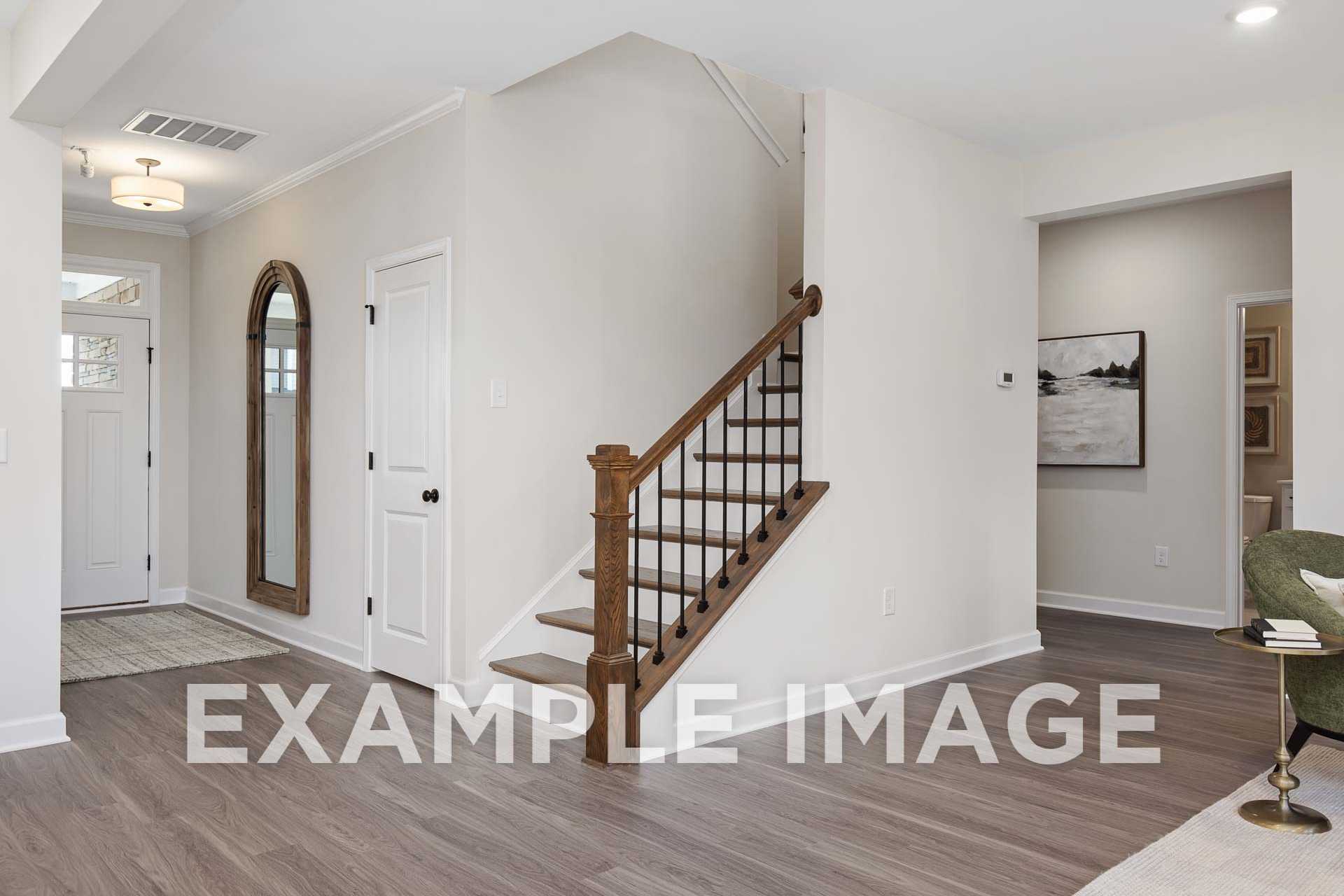 Spacious entry foyer in The Willow F home design featuring oak staircase, arched mirror, and hardwood floors