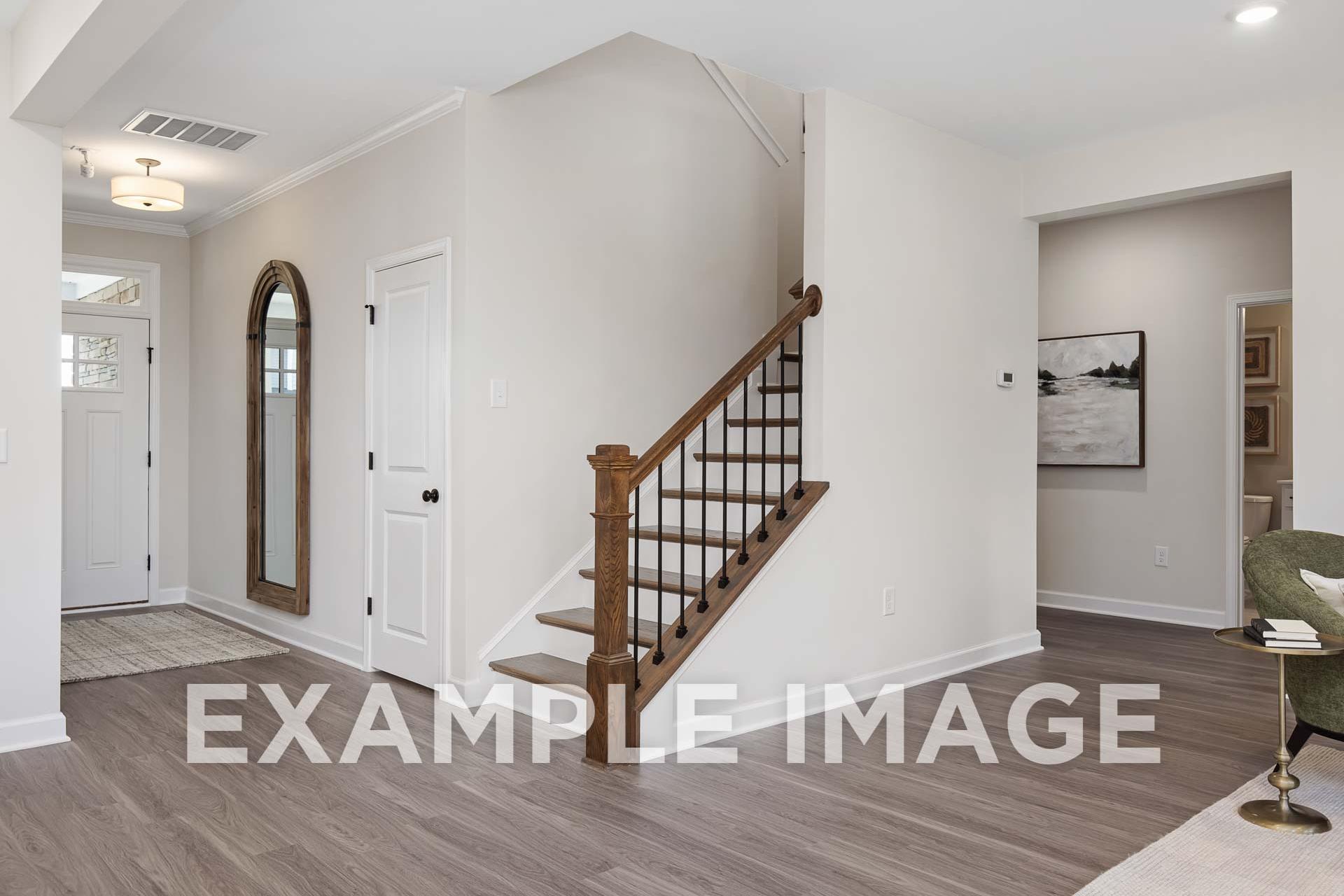 Spacious entry foyer in The Willow E 2-story home featuring wooden staircase, arched mirror, white walls, and hardwood floors