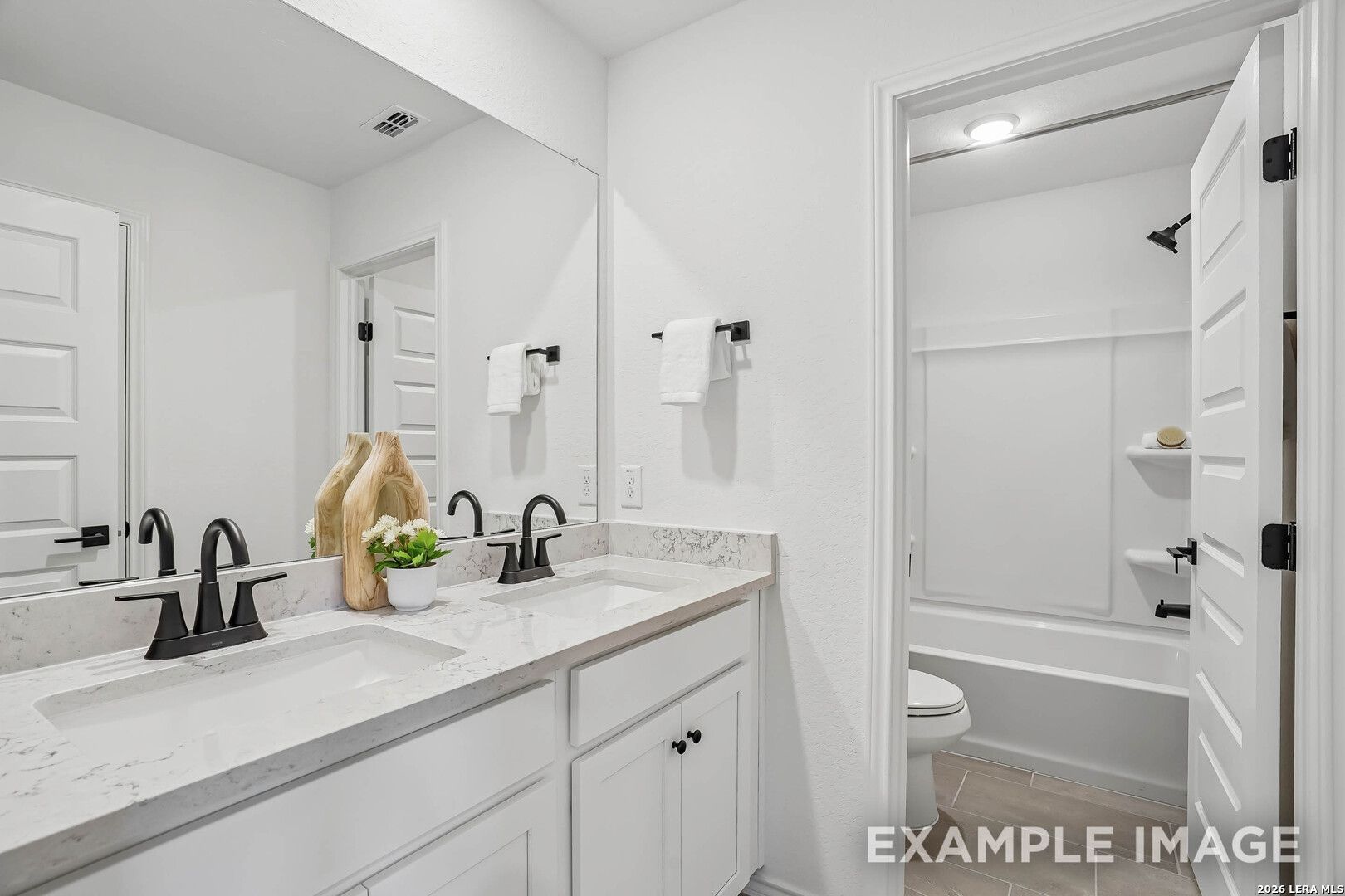 Bright white dual-vanity bathroom with marble countertops, matte black faucets, and tub shower in Davidson Homes Pinecrest E, Converse TX