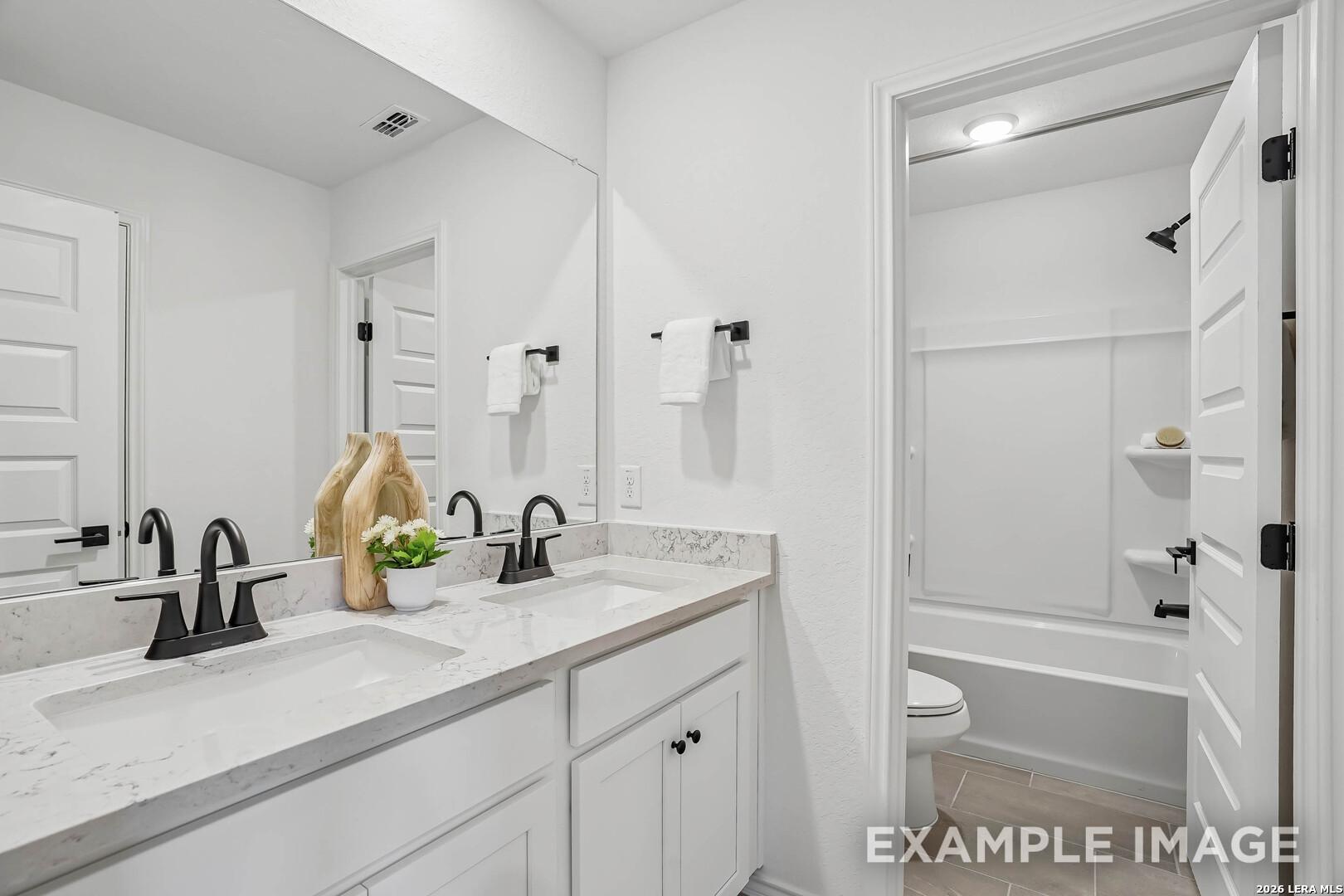 Double vanity bathroom with white cabinets, marble countertops, black fixtures, and tub shower combo in Davidson Homes Pinecrest F plan