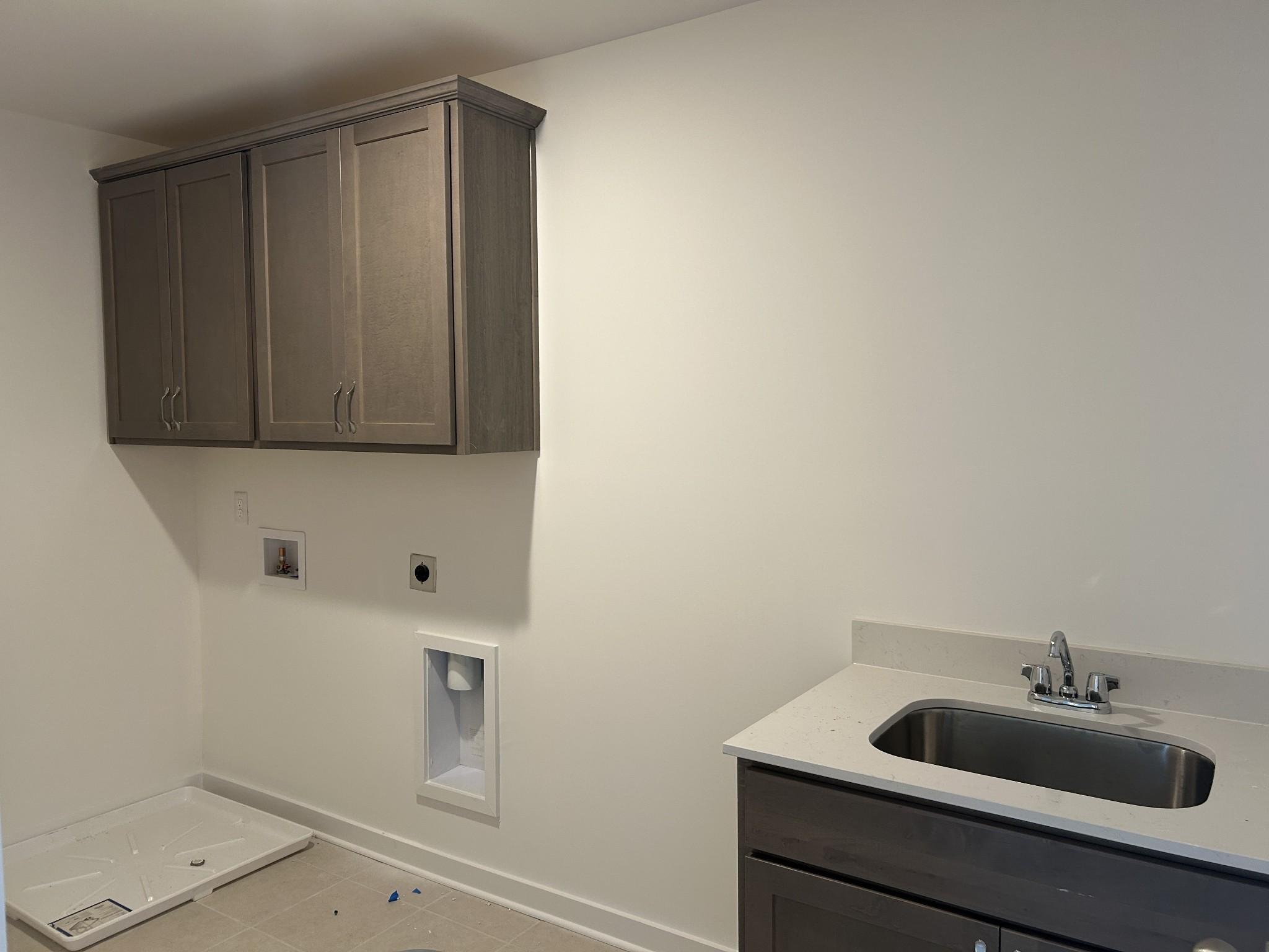 Modern laundry room featuring gray shaker cabinets, stainless utility sink, and washer-dryer hookups in Davidson Homes The Henry C, Mt. Juliet, TN