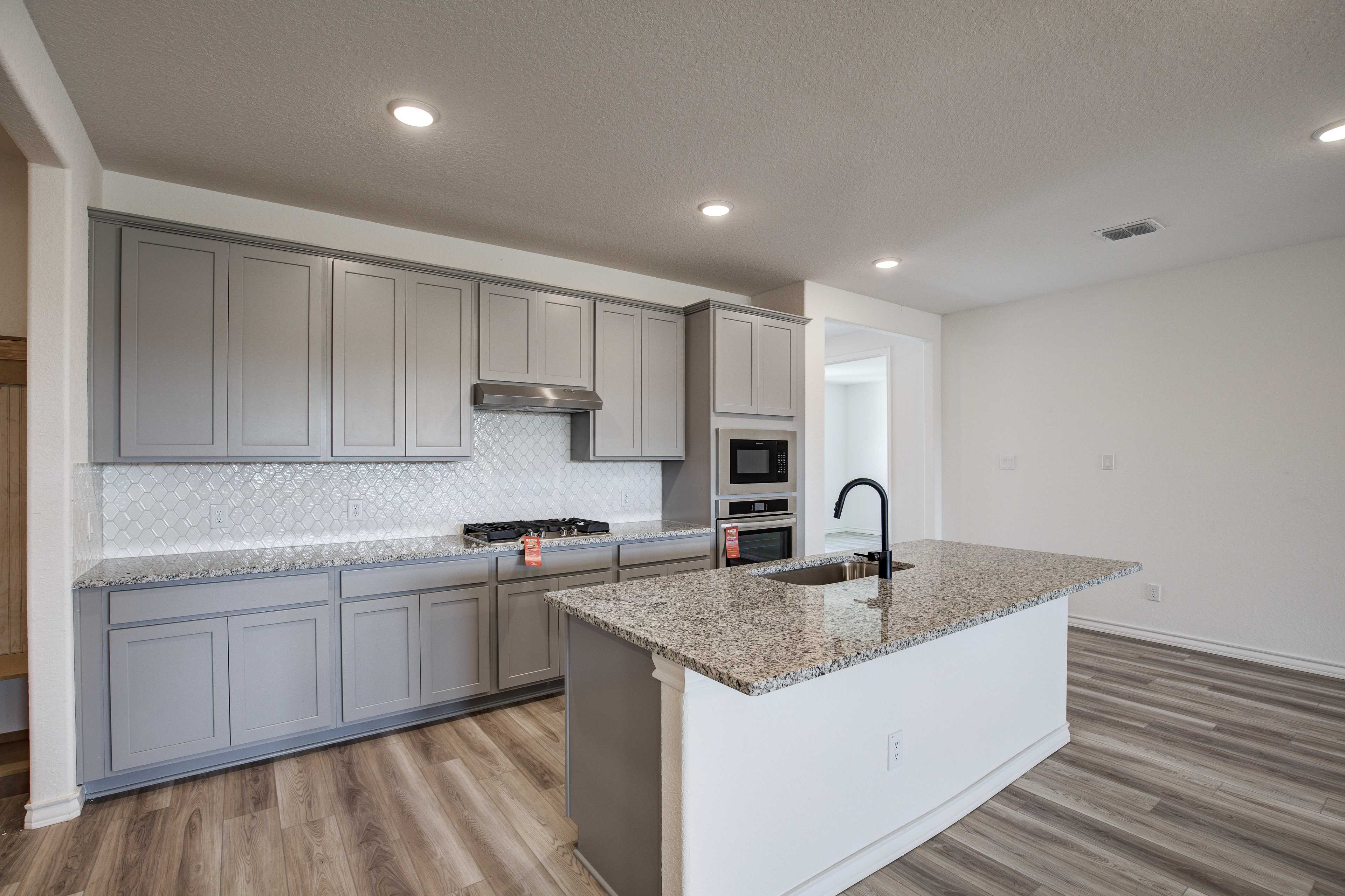 Spacious modern kitchen in The Lanier with gray shaker cabinets, granite island, stainless appliances, subway tile backsplash