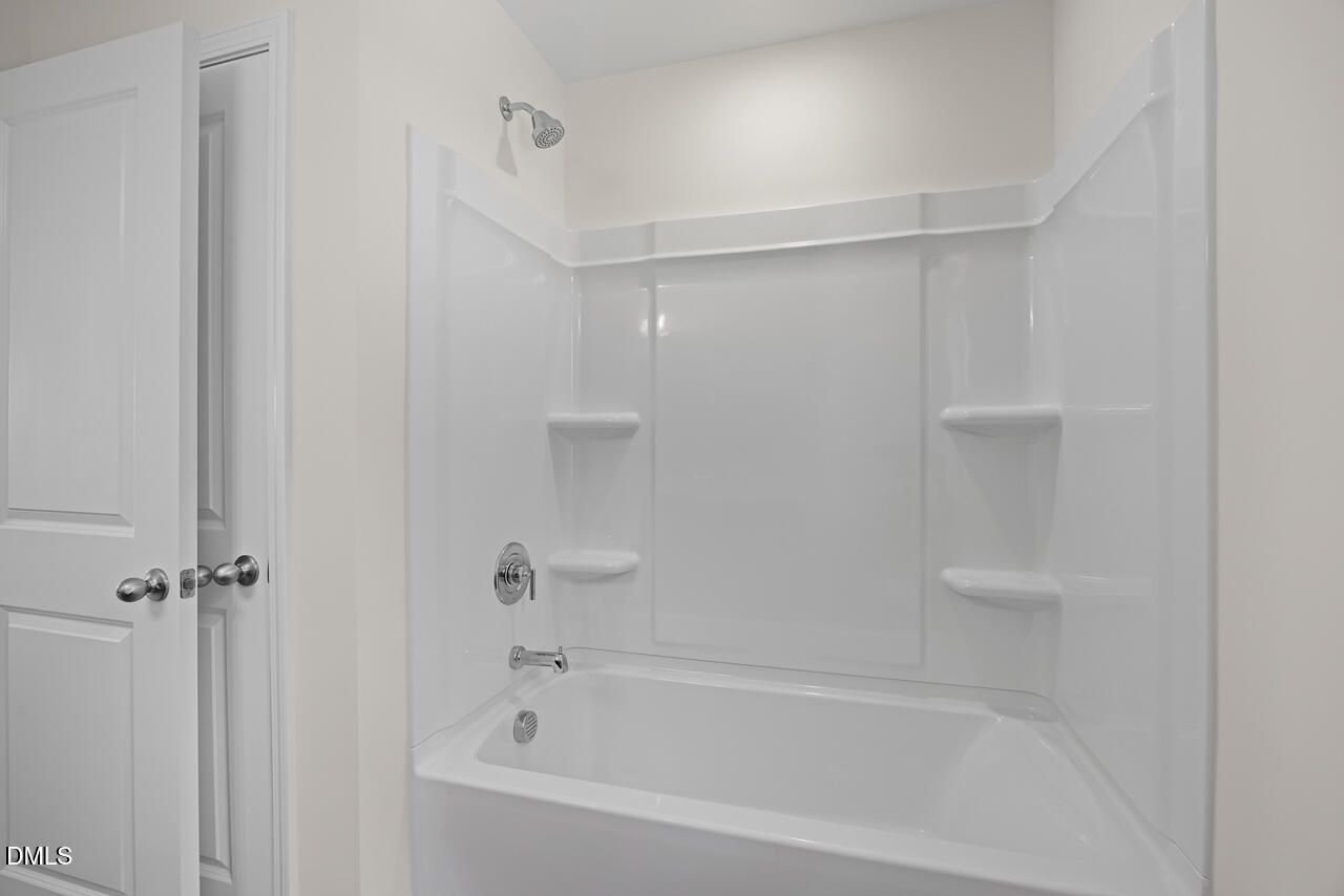 White bathtub with shower surround and built-in shelving in bathroom of Davidson Homes The Willow B, Zebulon, North Carolina