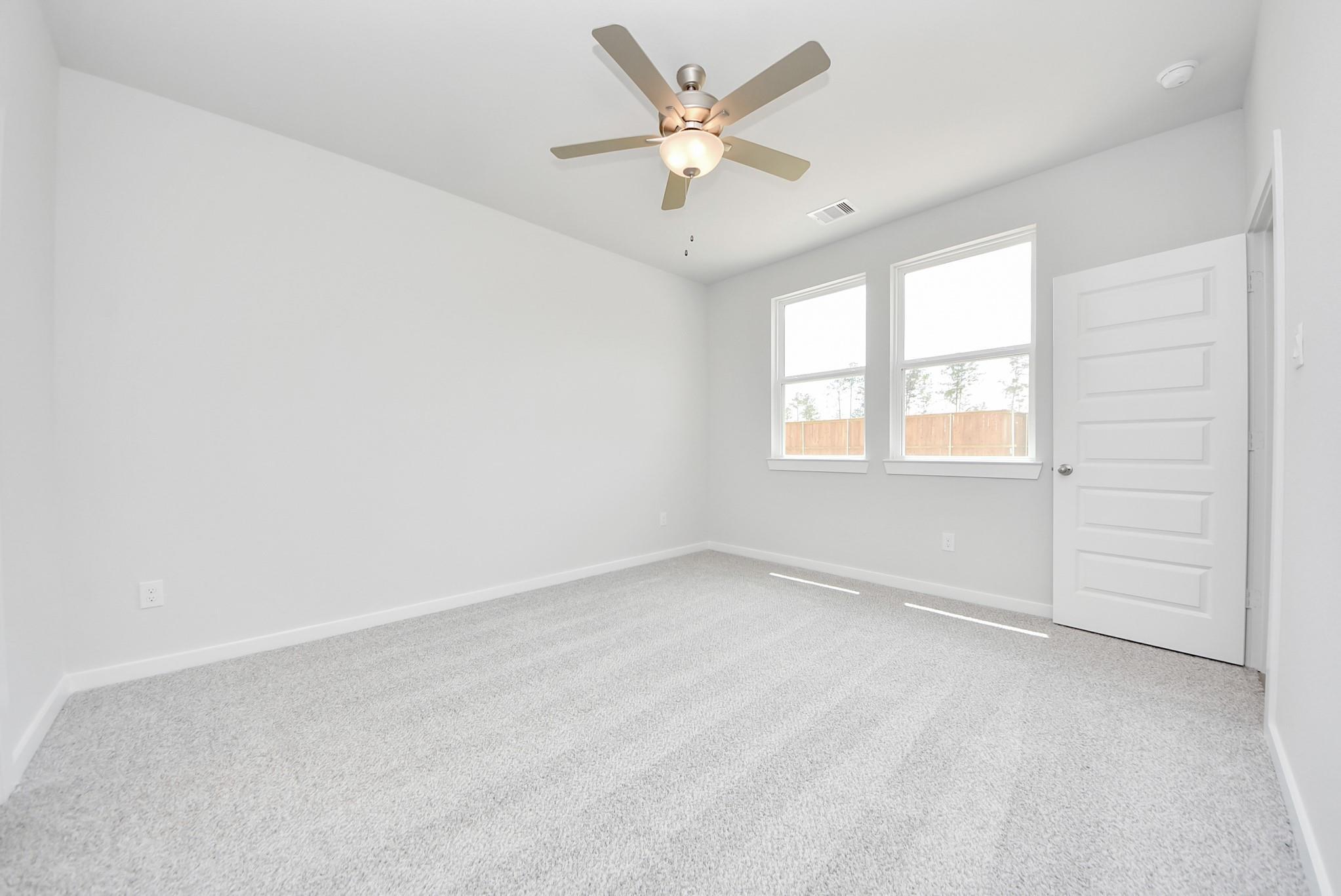 Bright, spacious bedroom with neutral carpet and ceiling fan in The Blanco F floor plan at Spring Branch Crossing, Conroe.