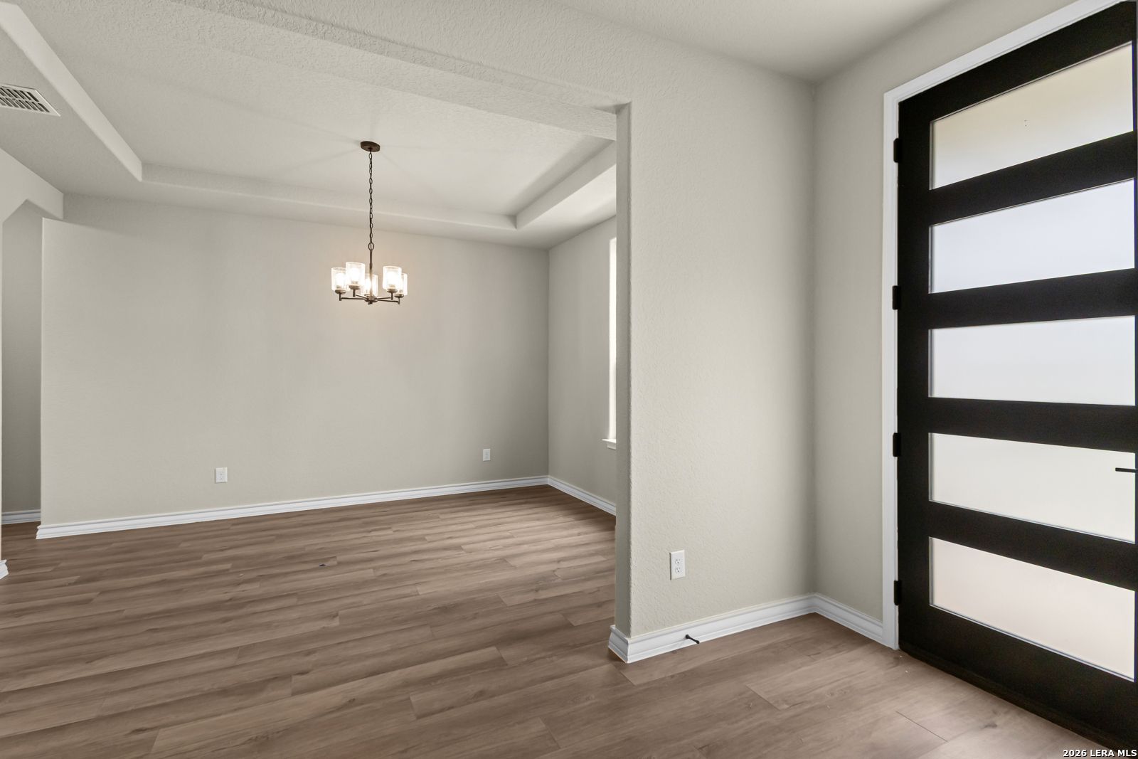 Formal dining room with tray ceiling and modern chandelier in The Danbury H model home at The Reserve at Potranco Oaks.