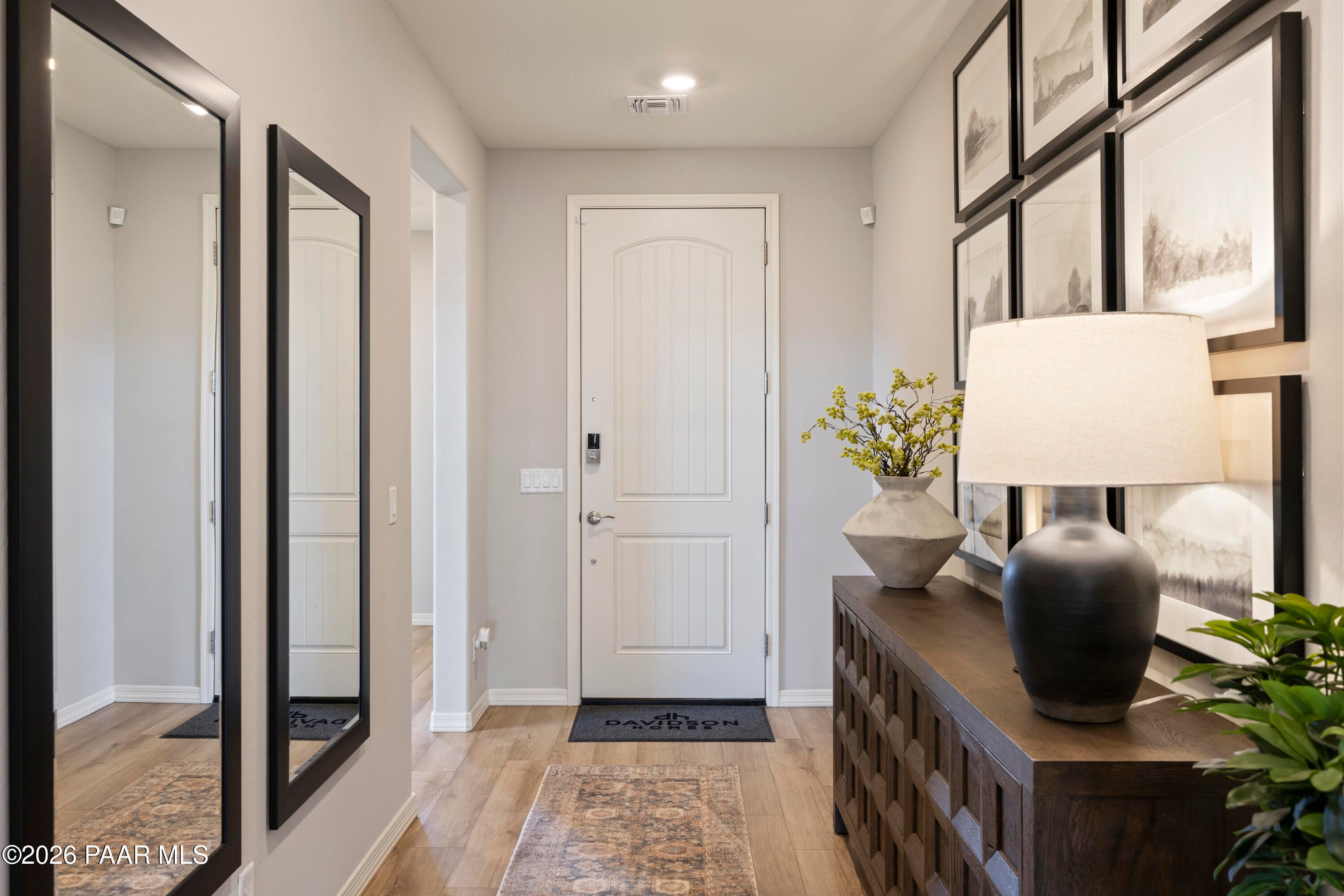 Elegant entryway with mirrored walls, white paneled door, hardwood floors, console table, and art in Davidson Homes The Harmony A, Prescott Valley, AZ