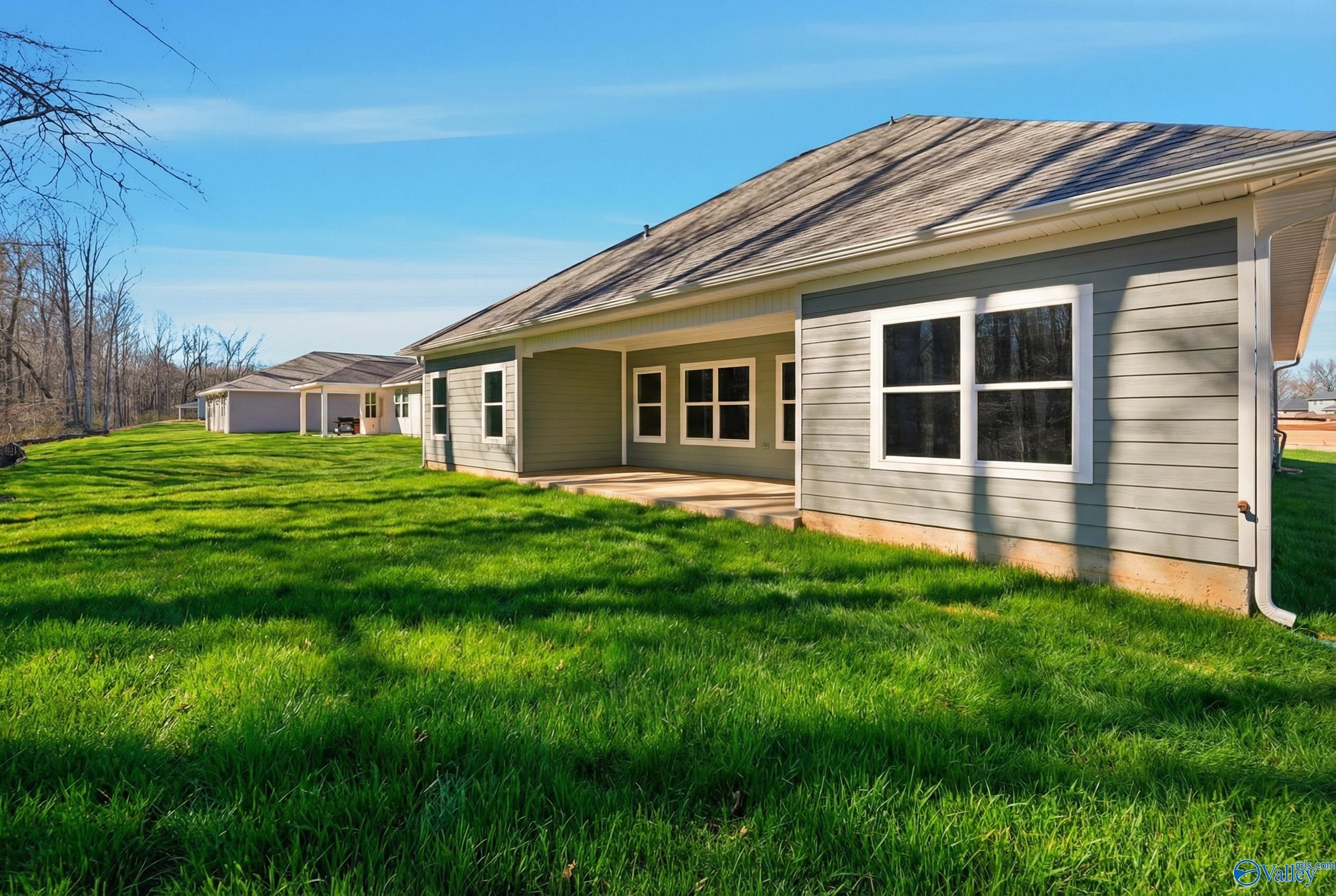Modern gray single-story home exterior with covered patio, large windows, and lush green lawn in Forest Glen, Hazel Green, Alabama