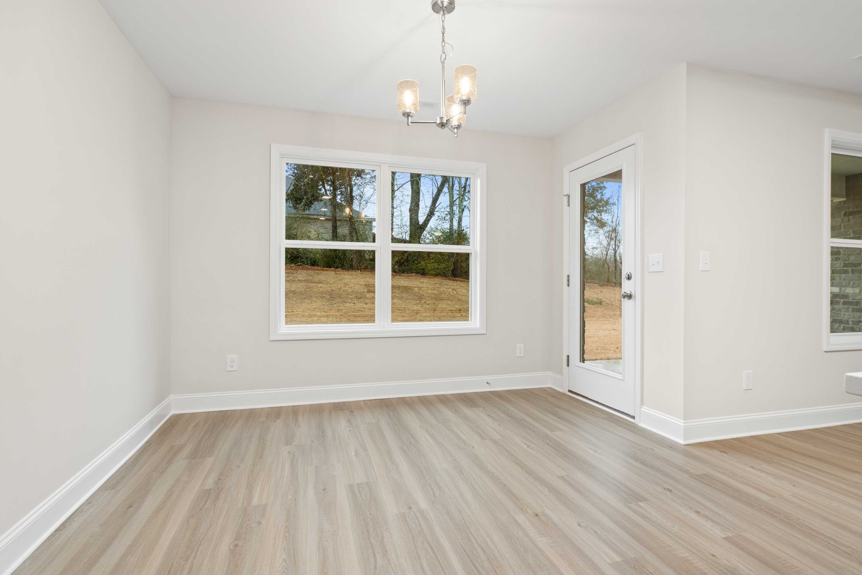 Spacious dining area in The Asheville home featuring large windows with backyard view, modern chandelier, and light wood flooring