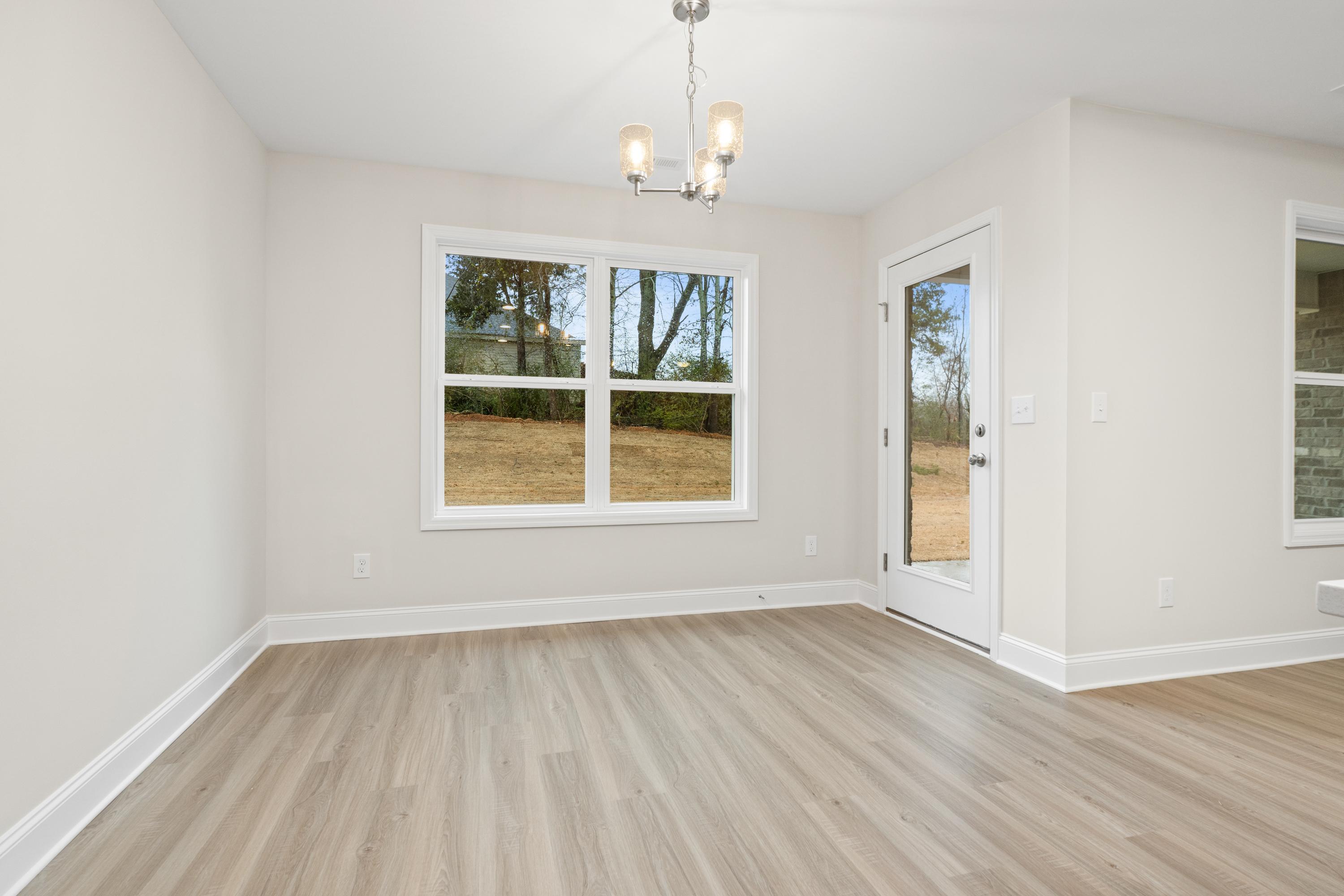 Spacious dining room in The Asheville by Davidson Homes featuring large window, glass patio door, and light oak luxury vinyl plank flooring