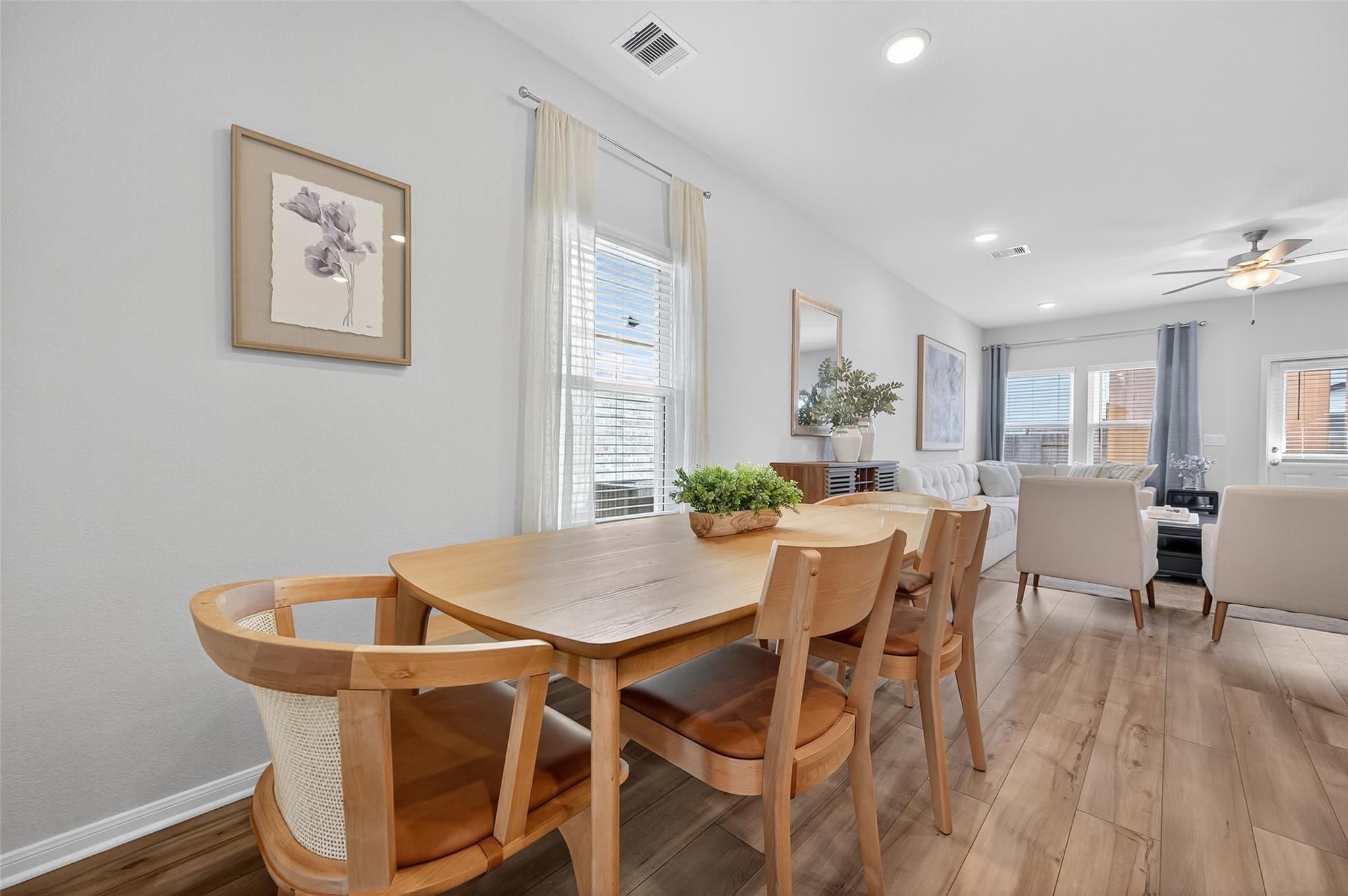 Modern dining room with oak table, rattan chairs, potted plants, and sheer curtains in The Brazos E by Davidson Homes, Magnolia, Texas